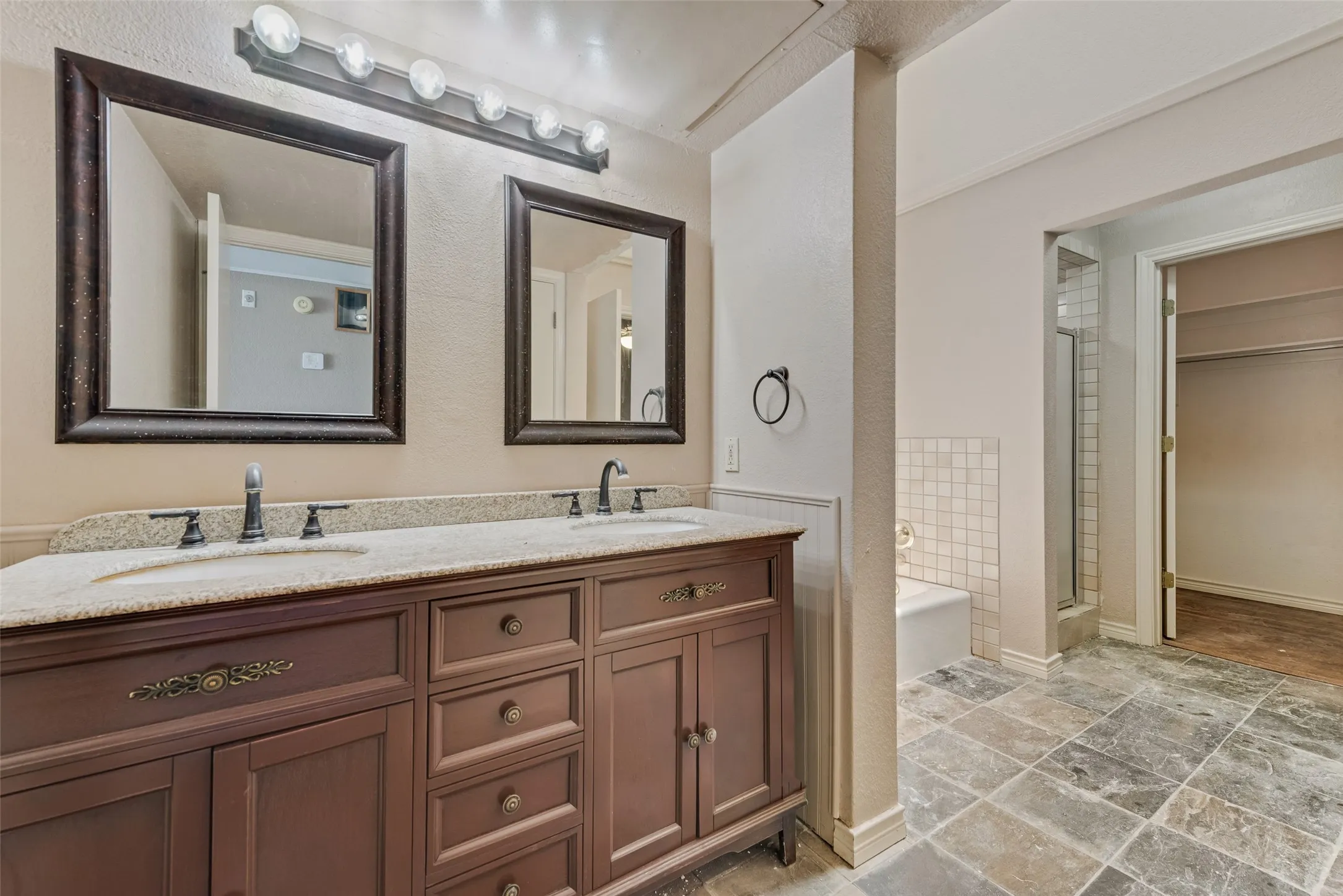 Bathroom featuring a bath, double vanity, a stall shower, light stone finish flooring, and a textured wall