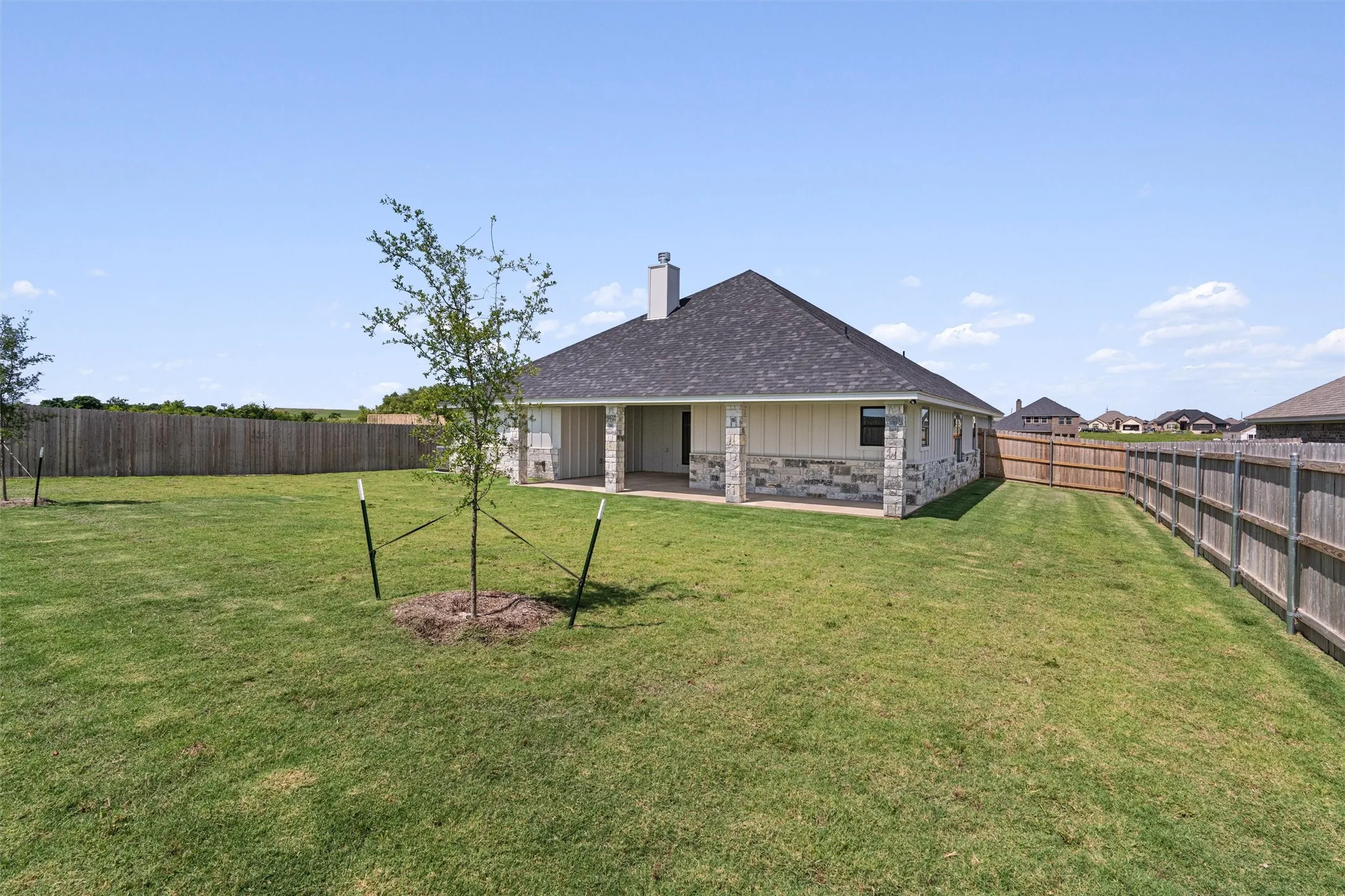 Expansive backyard featuring a manicured lawn, established privacy fencing, and a covered patio with stone columns