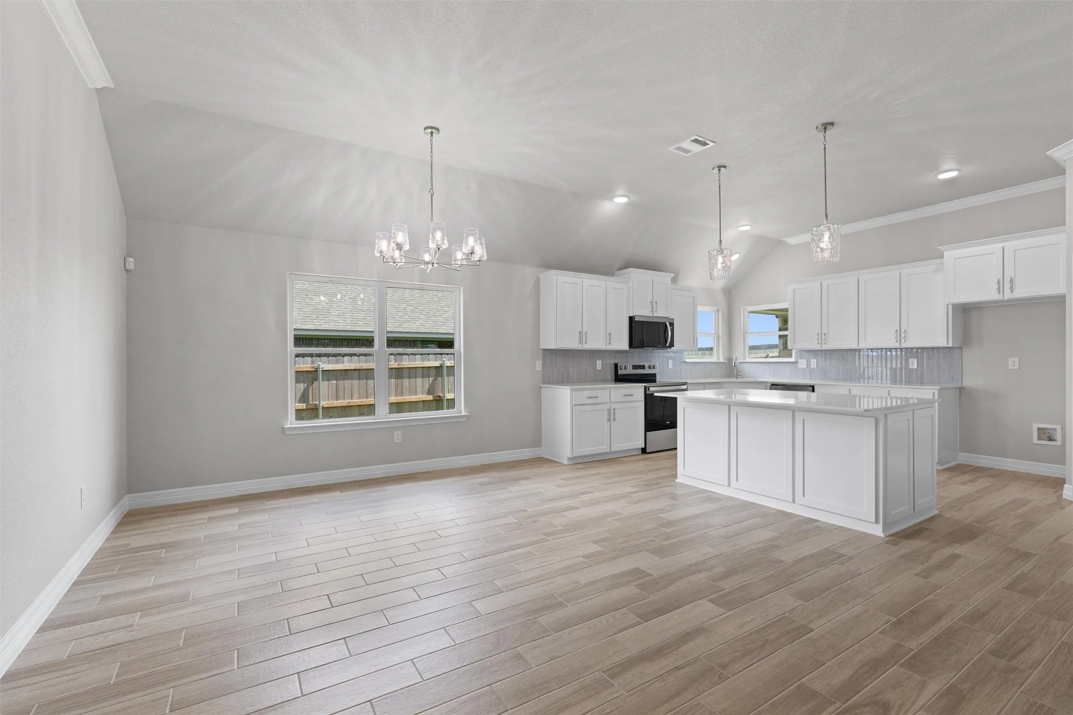 Open-concept living area with vaulted ceilings, wood-finish flooring, a contemporary chandelier, and a kitchen featuring white cabinetry, a large island, and stainless steel appliances