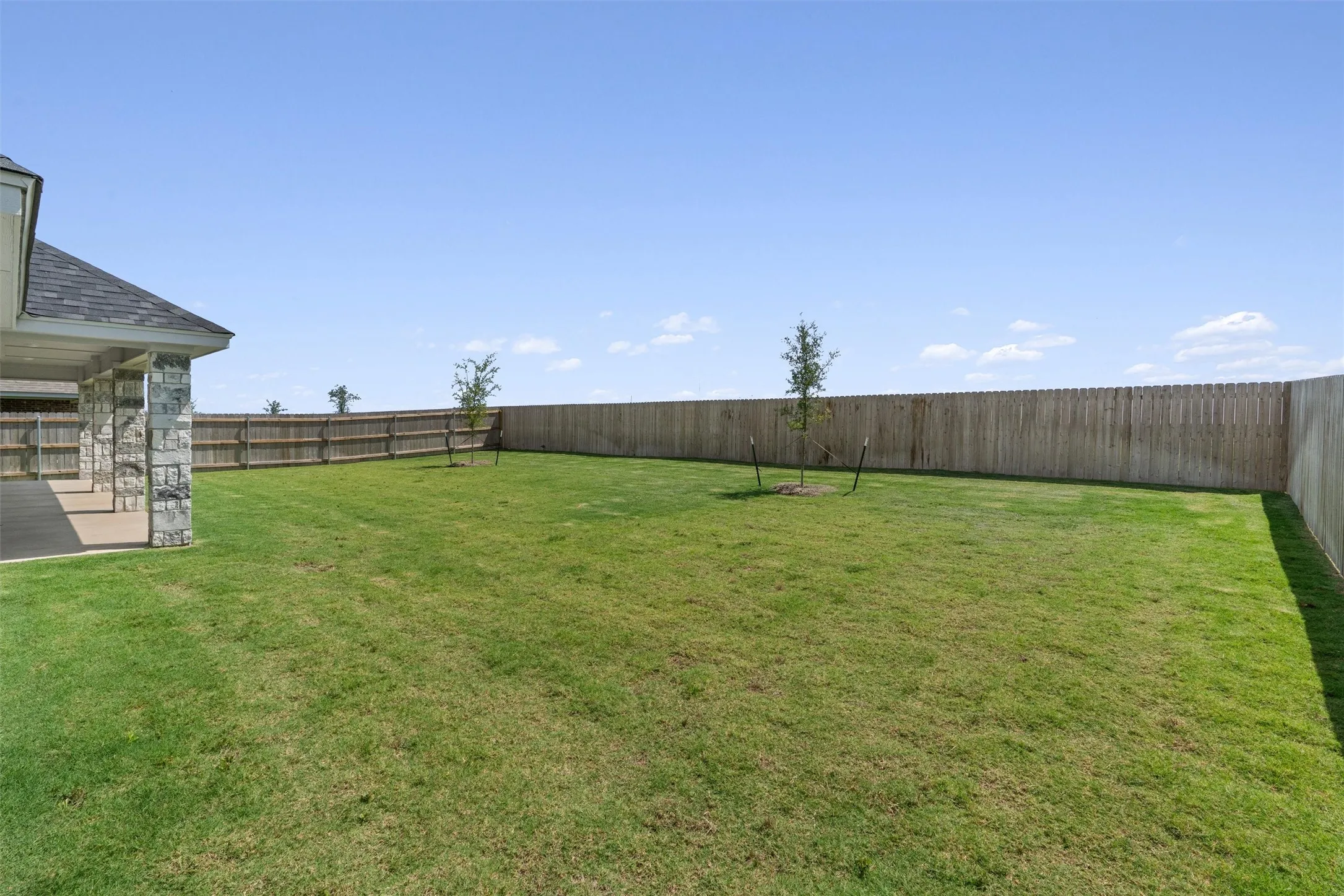 Expansive private backyard featuring a full perimeter wooden fence, a manicured green lawn, and two young trees