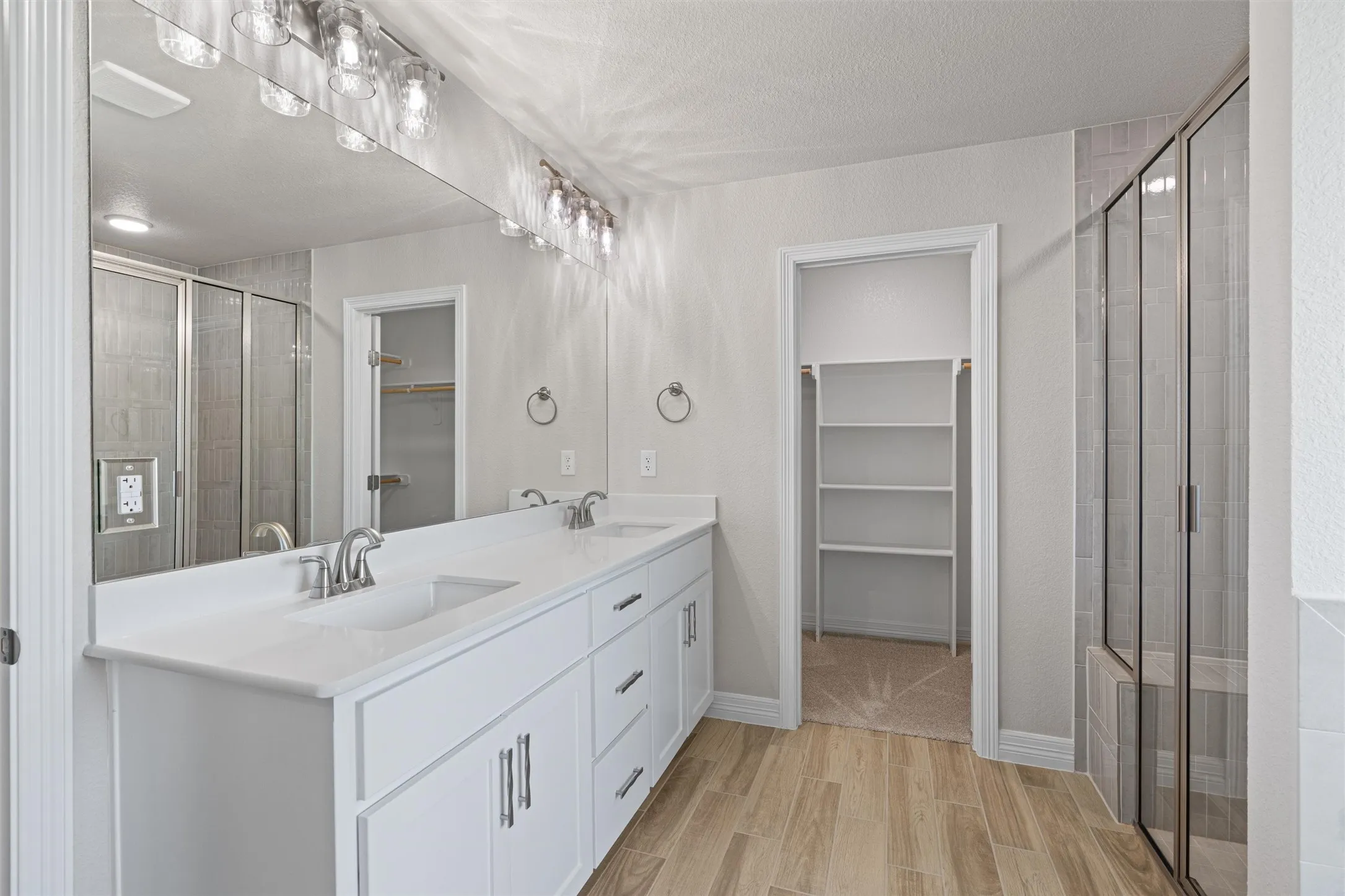 Dual vanity with white cabinetry and integrated sinks, a large frameless mirror, and overhead decorative lighting