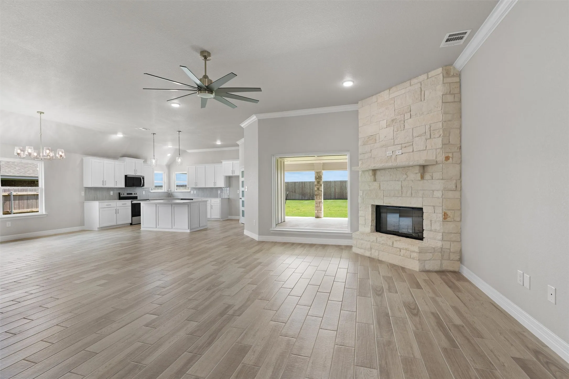 Spacious open-concept interior featuring light wood-finish flooring and a corner stone fireplace