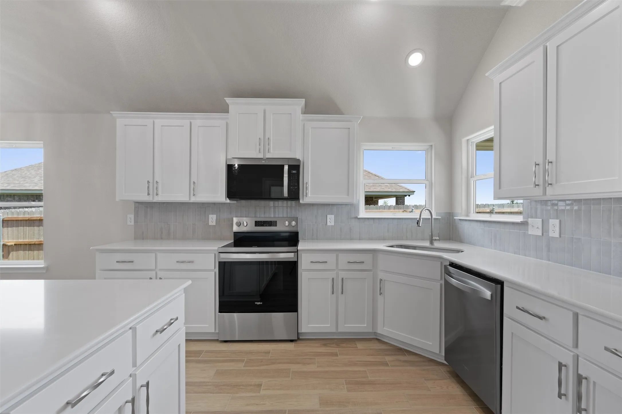 Modern kitchen featuring white cabinetry, light countertops, wood-finish flooring, a tiled backsplash, and stainless steel appliances