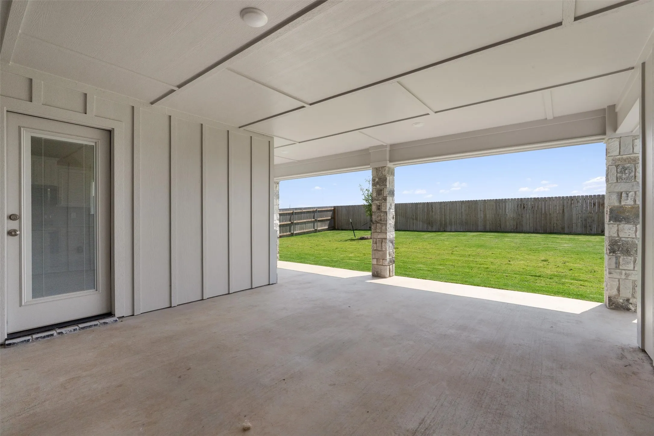 Expansive covered patio featuring a concrete surface, overhead lighting, and stone-clad columns