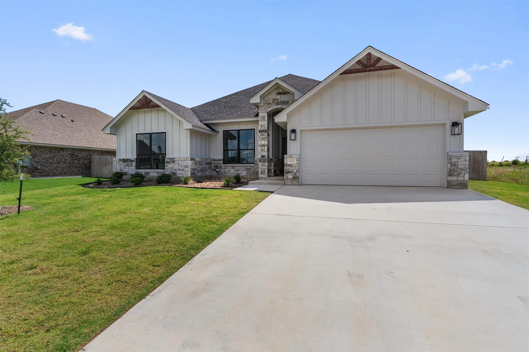 Contemporary single-story residence featuring a two-car garage, board and batten siding, stone accents, and a concrete driveway