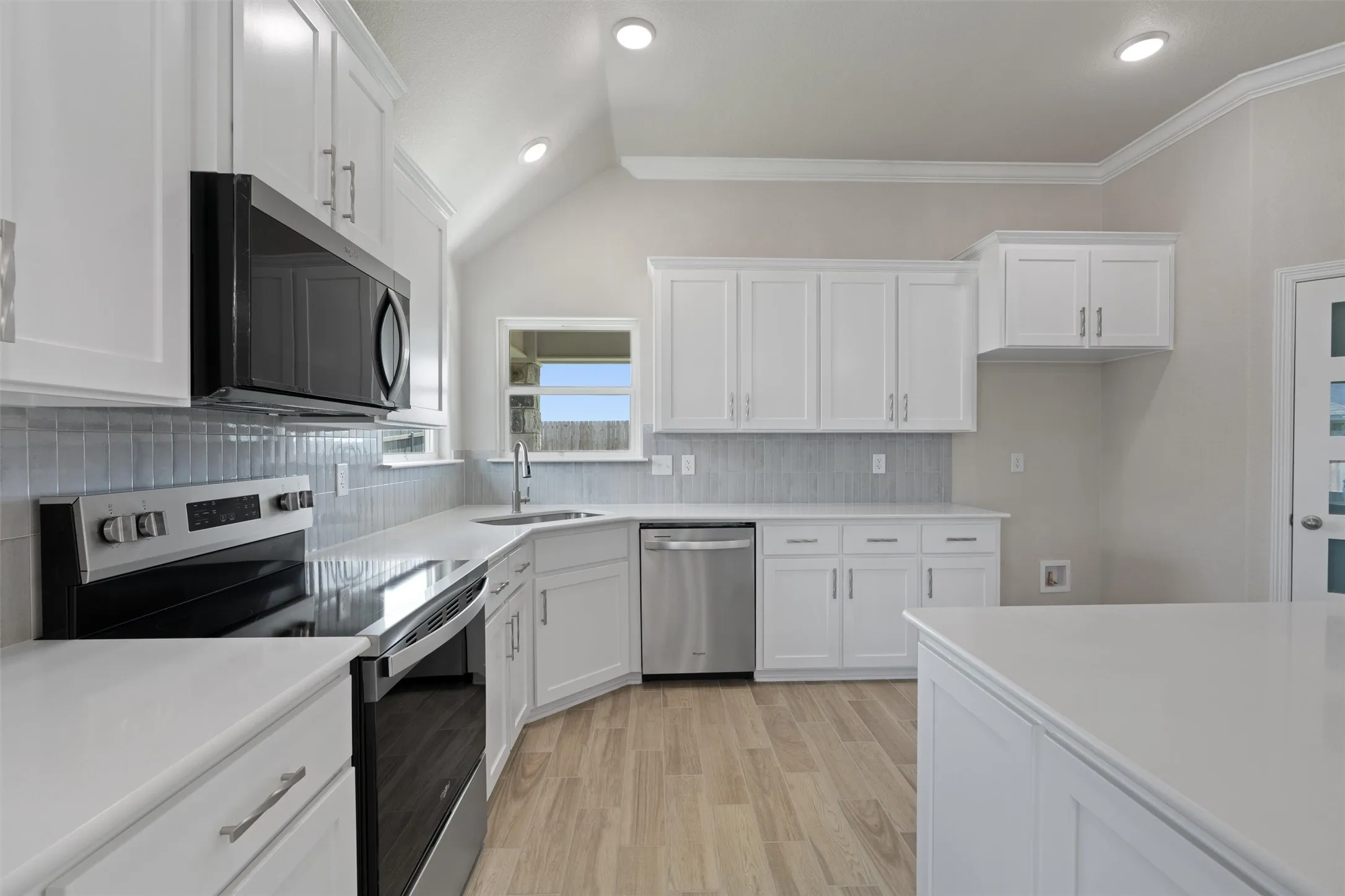 Bright kitchen featuring white cabinetry, light countertops, stainless steel appliances, a tile backsplash, and light wood-finish flooring