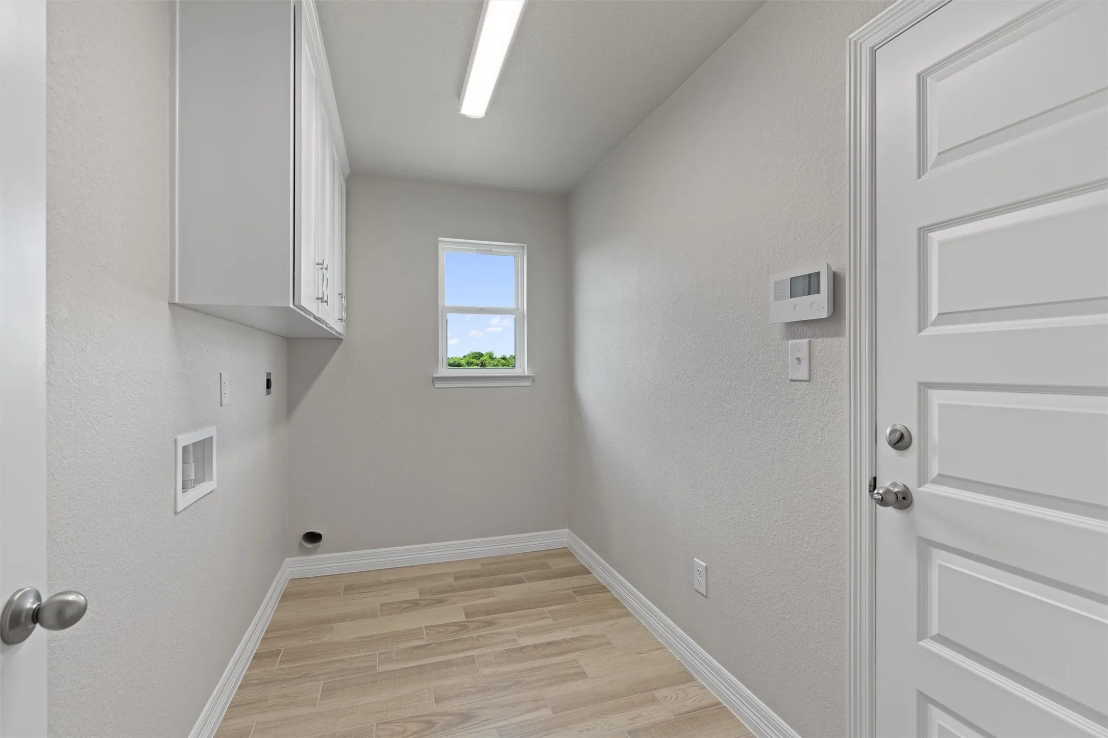 Utility room featuring wood-finish flooring, white cabinetry, a single window, and a paneled door