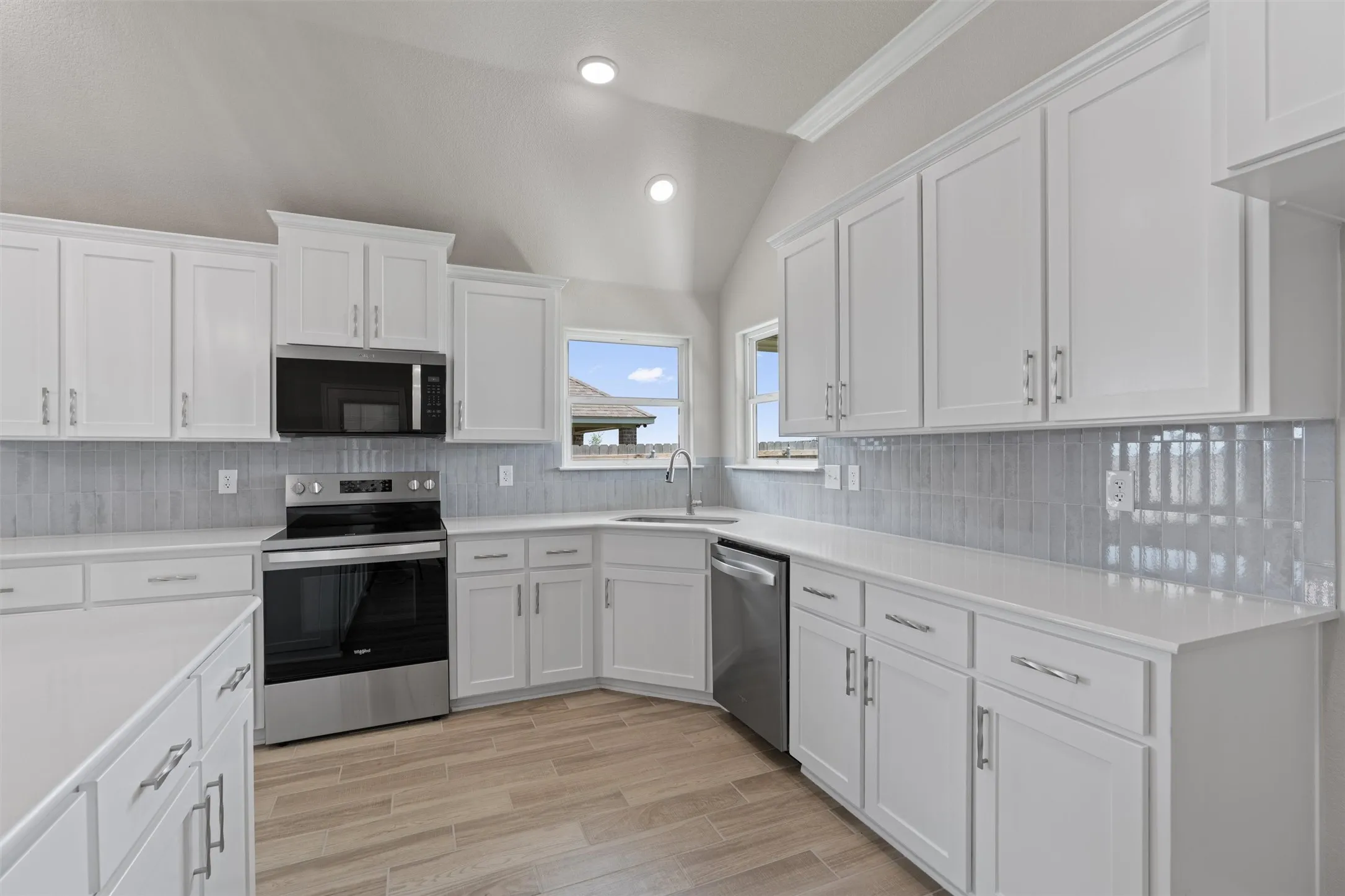 Modern kitchen featuring white shaker cabinetry with brushed nickel hardware, light countertops, and a gray subway tile backsplash