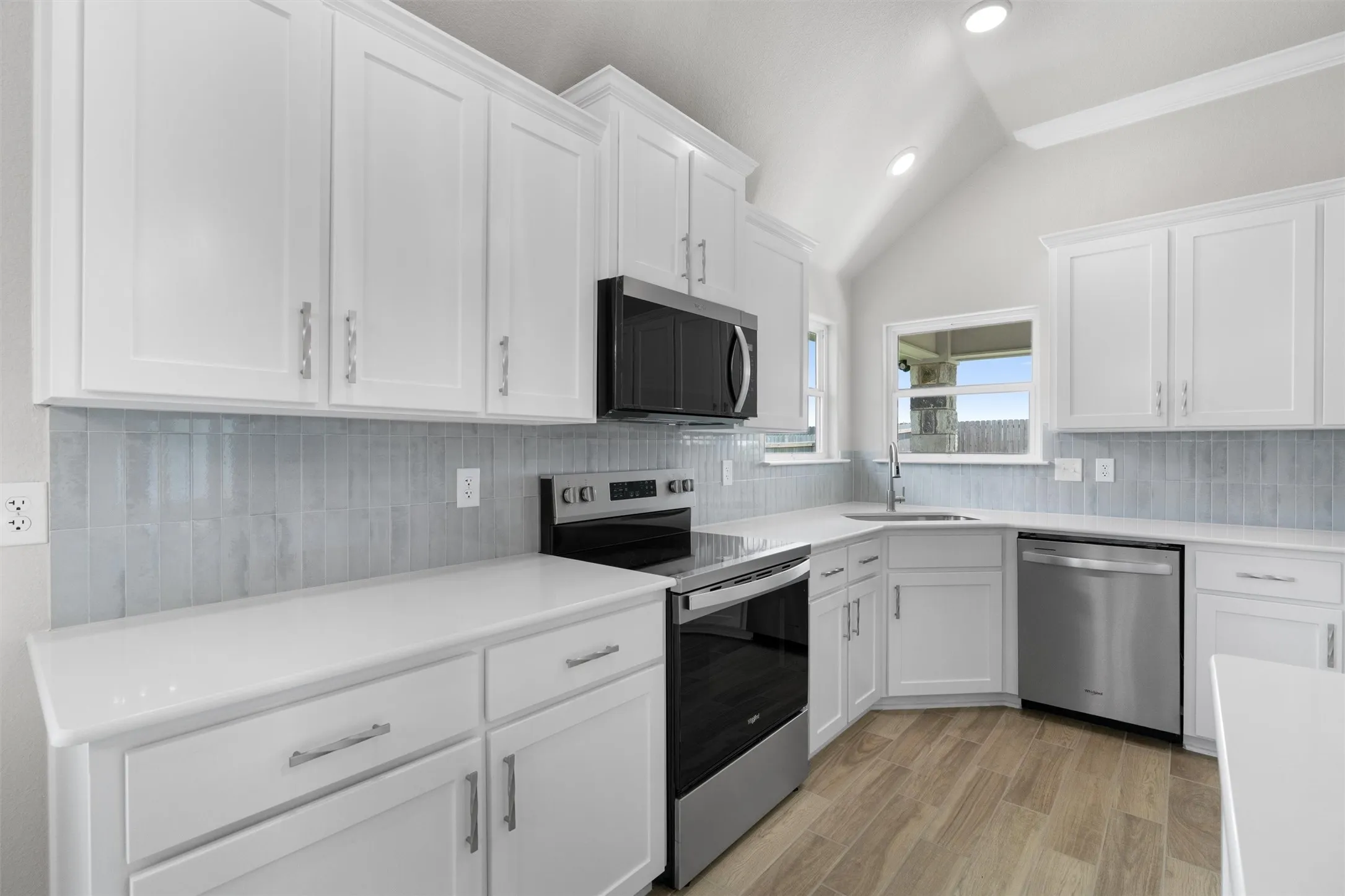 Kitchen featuring vaulted ceilings, recessed lighting, white cabinetry, stainless steel appliances, and wood-finish flooring