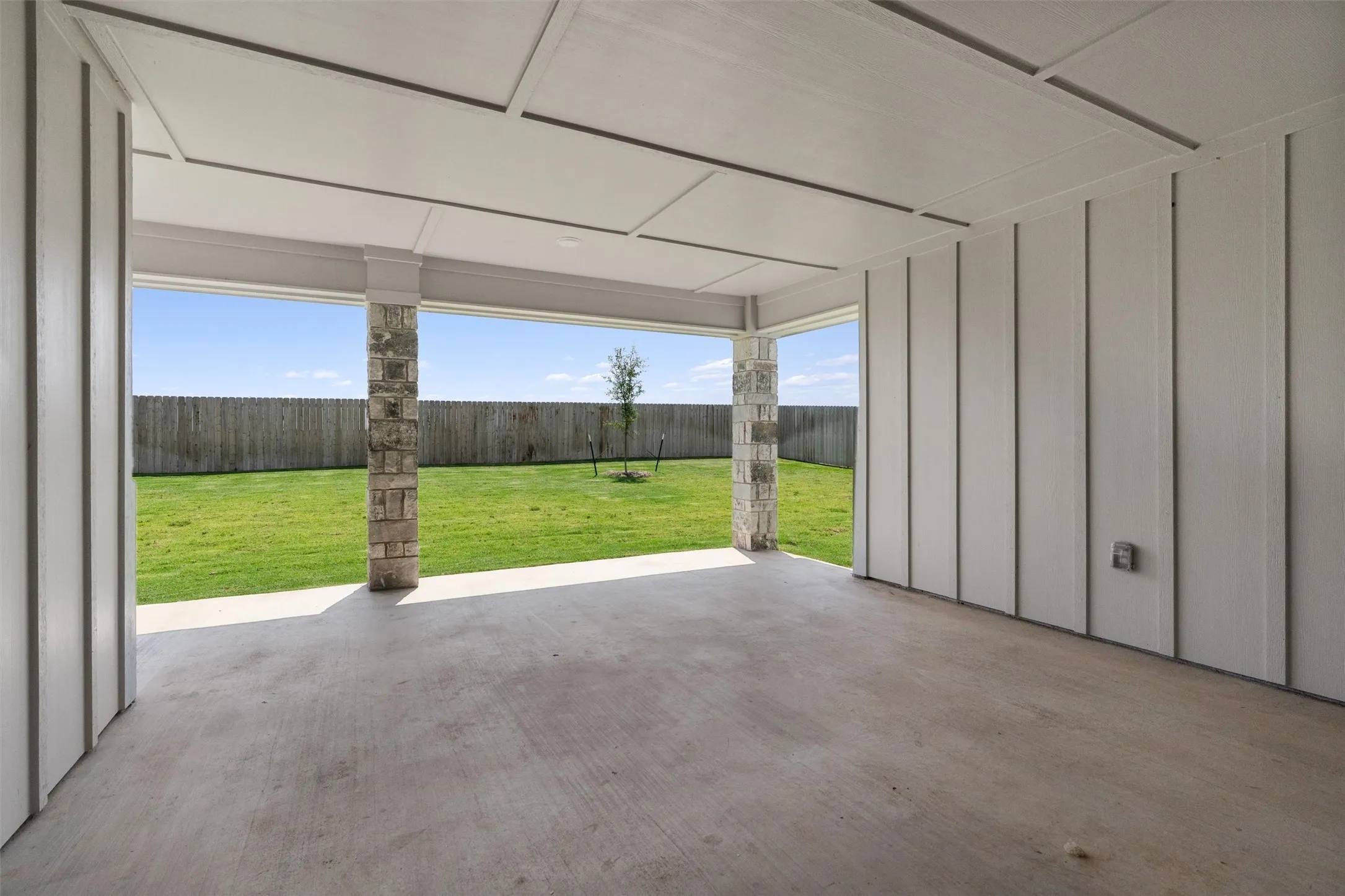 Covered patio featuring a concrete floor, stone columns, and paneling on the walls and ceiling