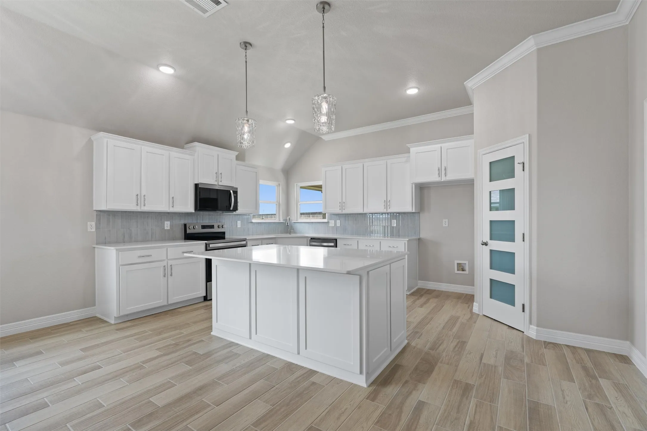 Spacious kitchen featuring an island, white shaker cabinetry, light-toned countertops, tile backsplash, and wood-finish flooring