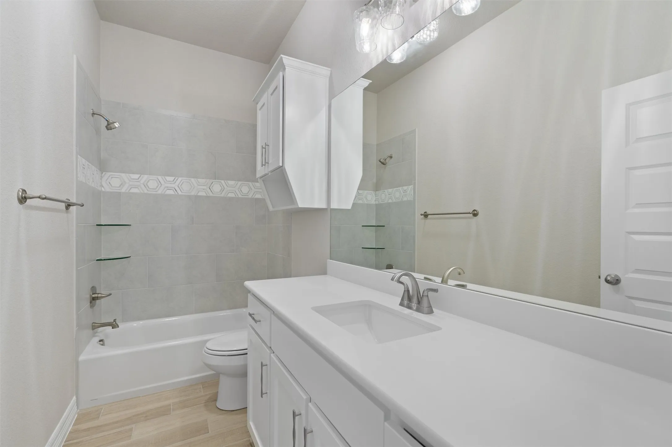 Bathroom featuring a single vanity with an integrated sink, a large wall mirror, and a tub with a tiled surround