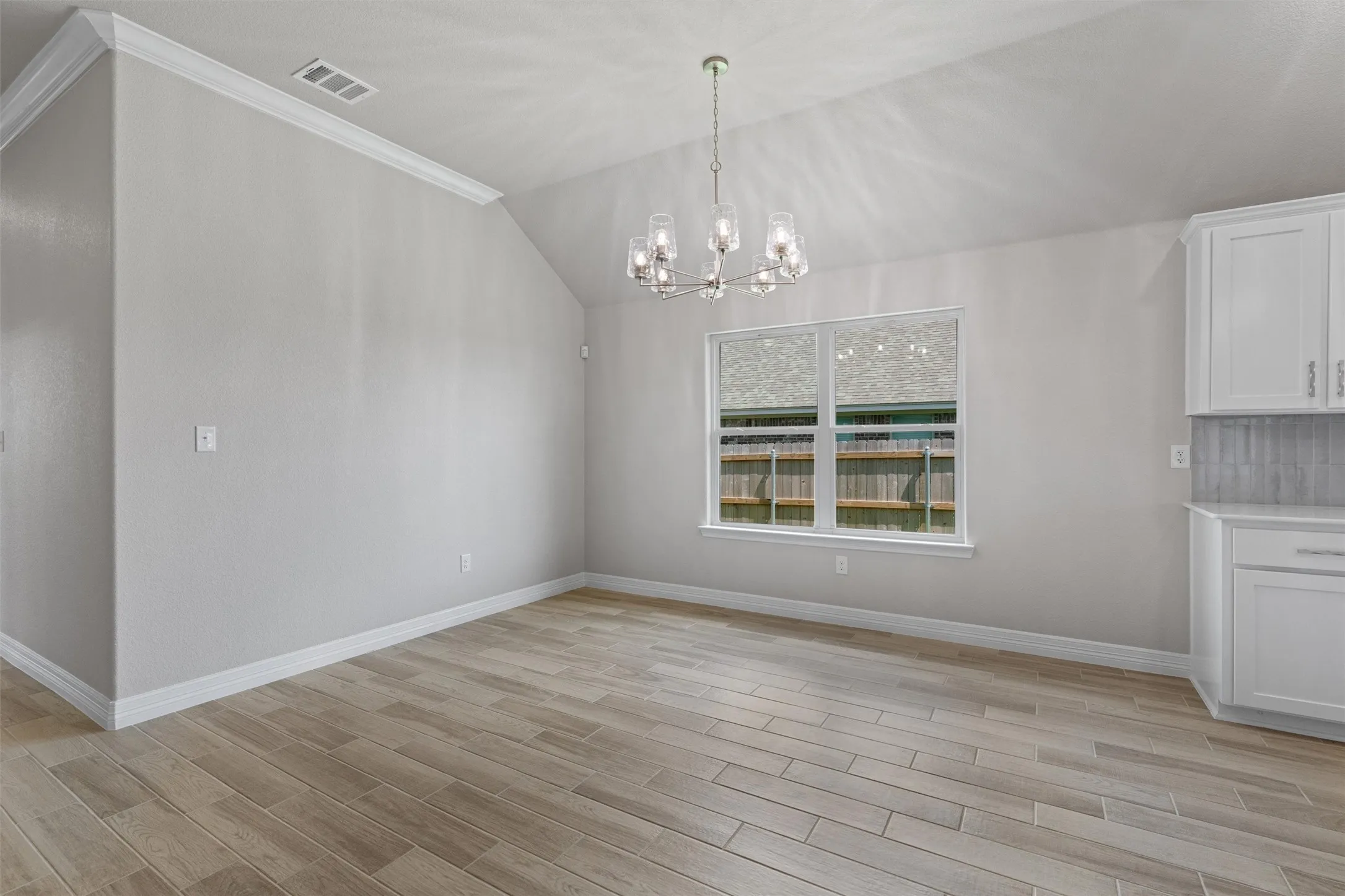 Spacious room featuring wood-finish flooring, vaulted ceiling, and a modern chandelier