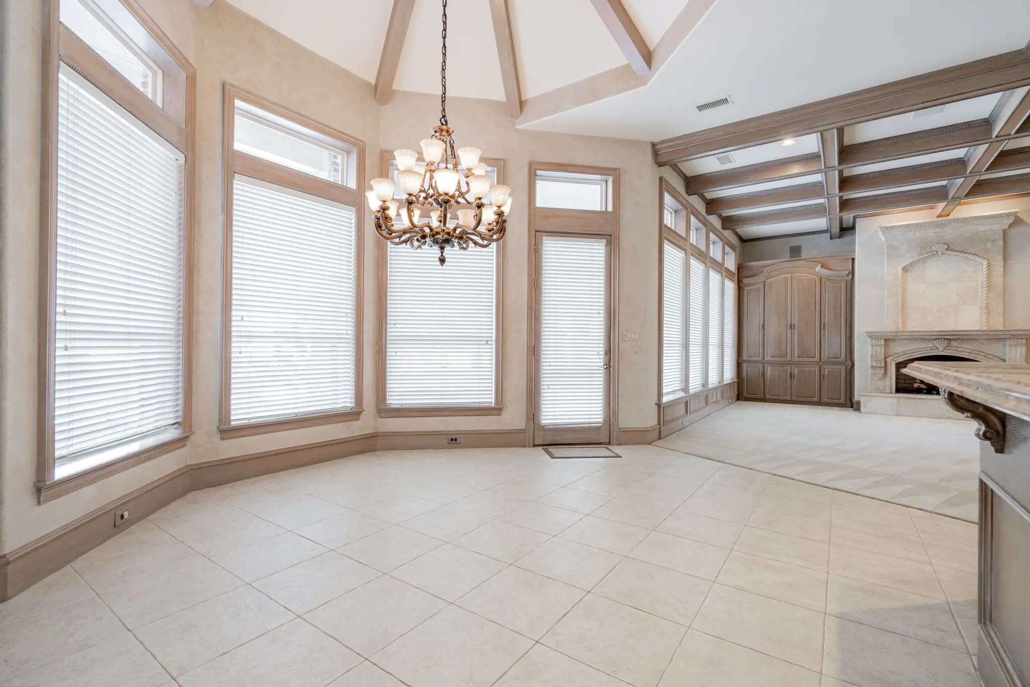 Unfurnished dining area with beam ceiling, light tile patterned floors, a high end fireplace, a chandelier, and coffered ceiling