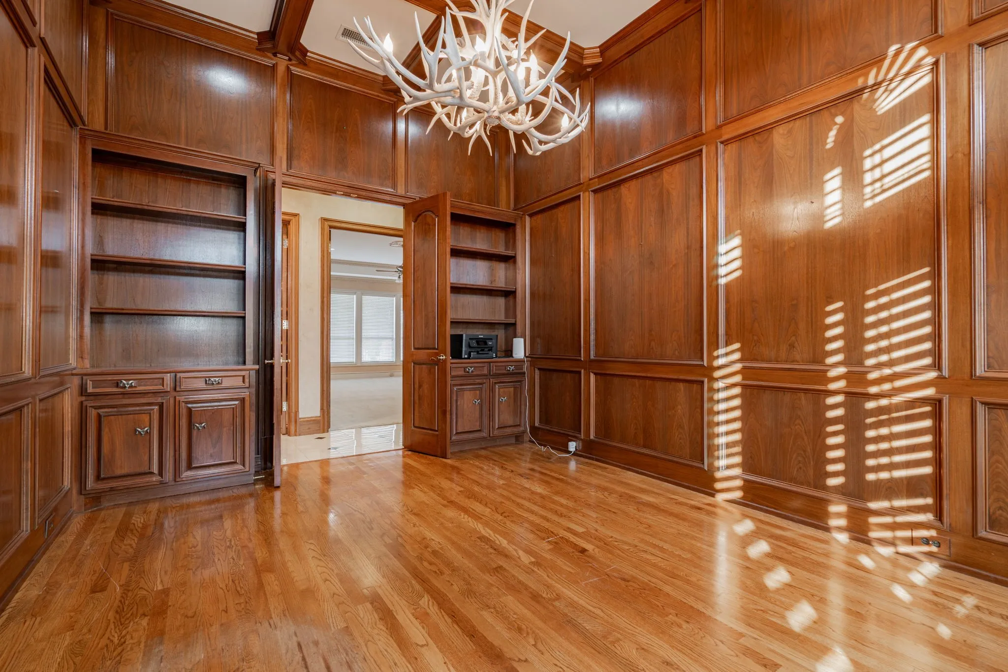 Unfurnished office with wood walls, built in shelves, a towering ceiling, a chandelier, and light wood-style floors