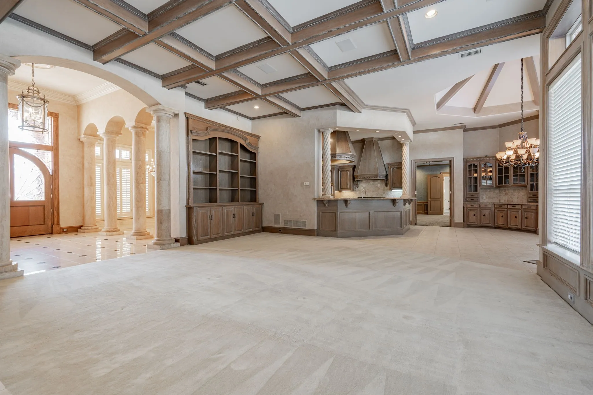 Unfurnished living room with a chandelier, arched walkways, decorative columns, beam ceiling, and coffered ceiling