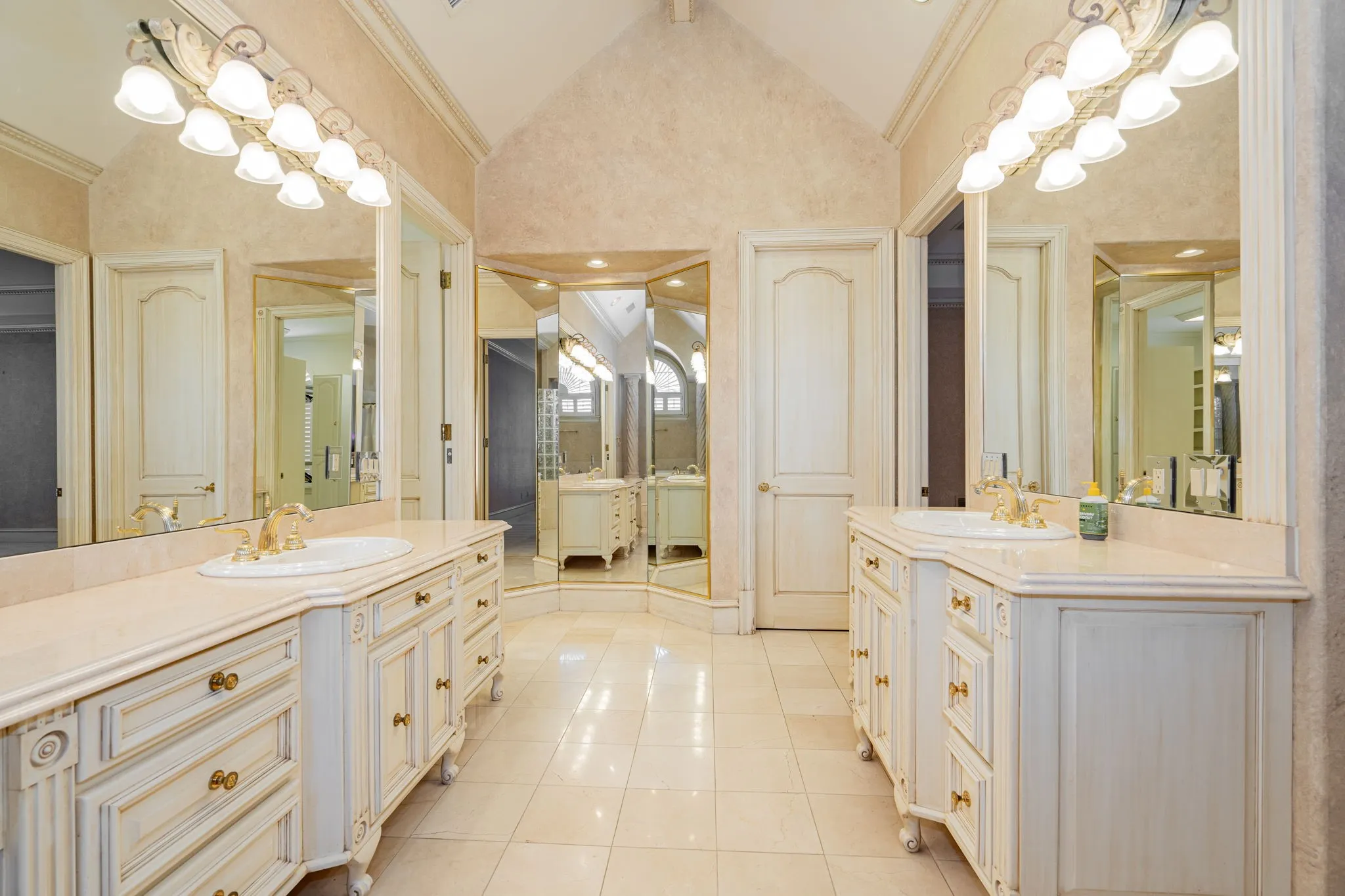 Full bathroom with two vanities, light tile patterned floors, high vaulted ceiling, and ornamental molding