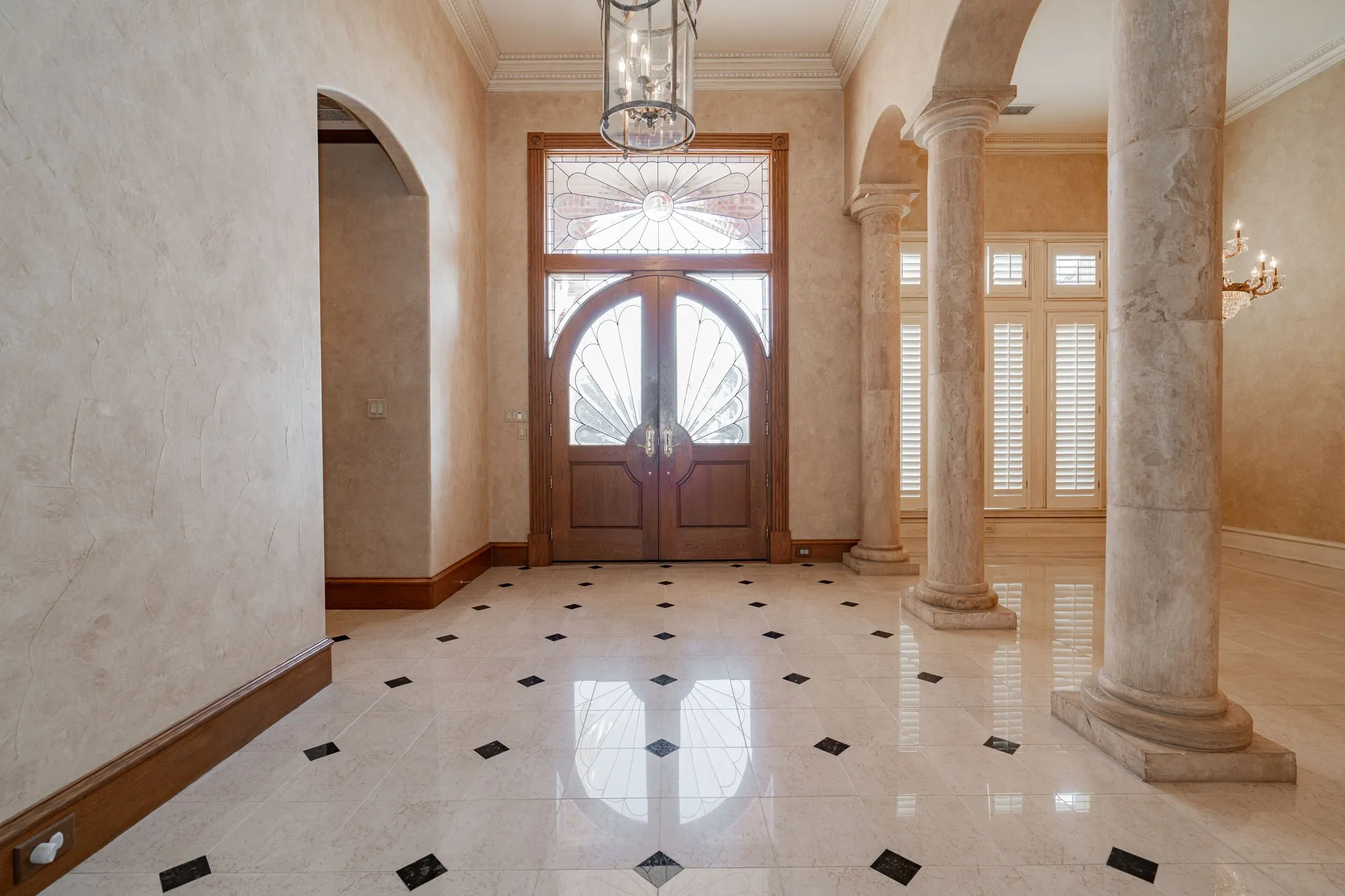Entrance foyer with ornate columns, arched walkways, a chandelier, ornamental molding, and inlaid floor details