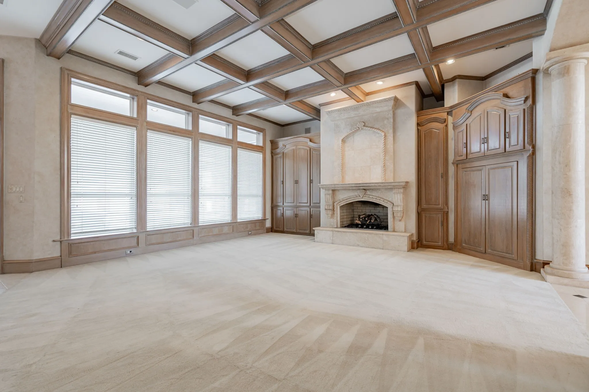 Unfurnished living room with beamed ceiling, light colored carpet, coffered ceiling, and a premium fireplace