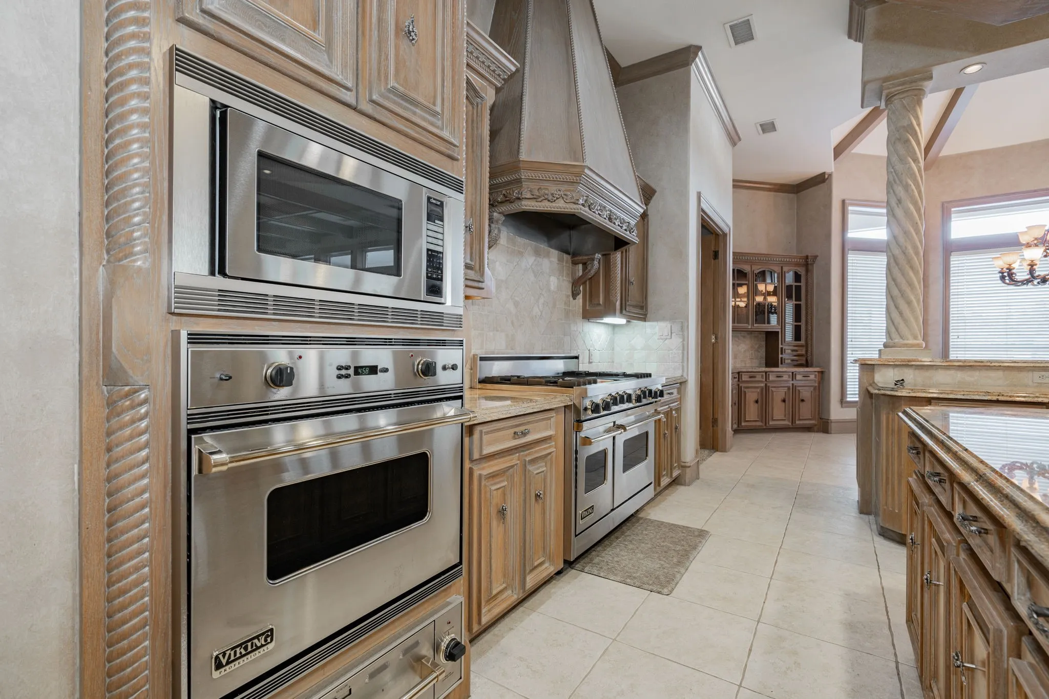 Kitchen with appliances with stainless steel finishes, glass insert cabinets, custom exhaust hood, tasteful backsplash, and light tile patterned floors