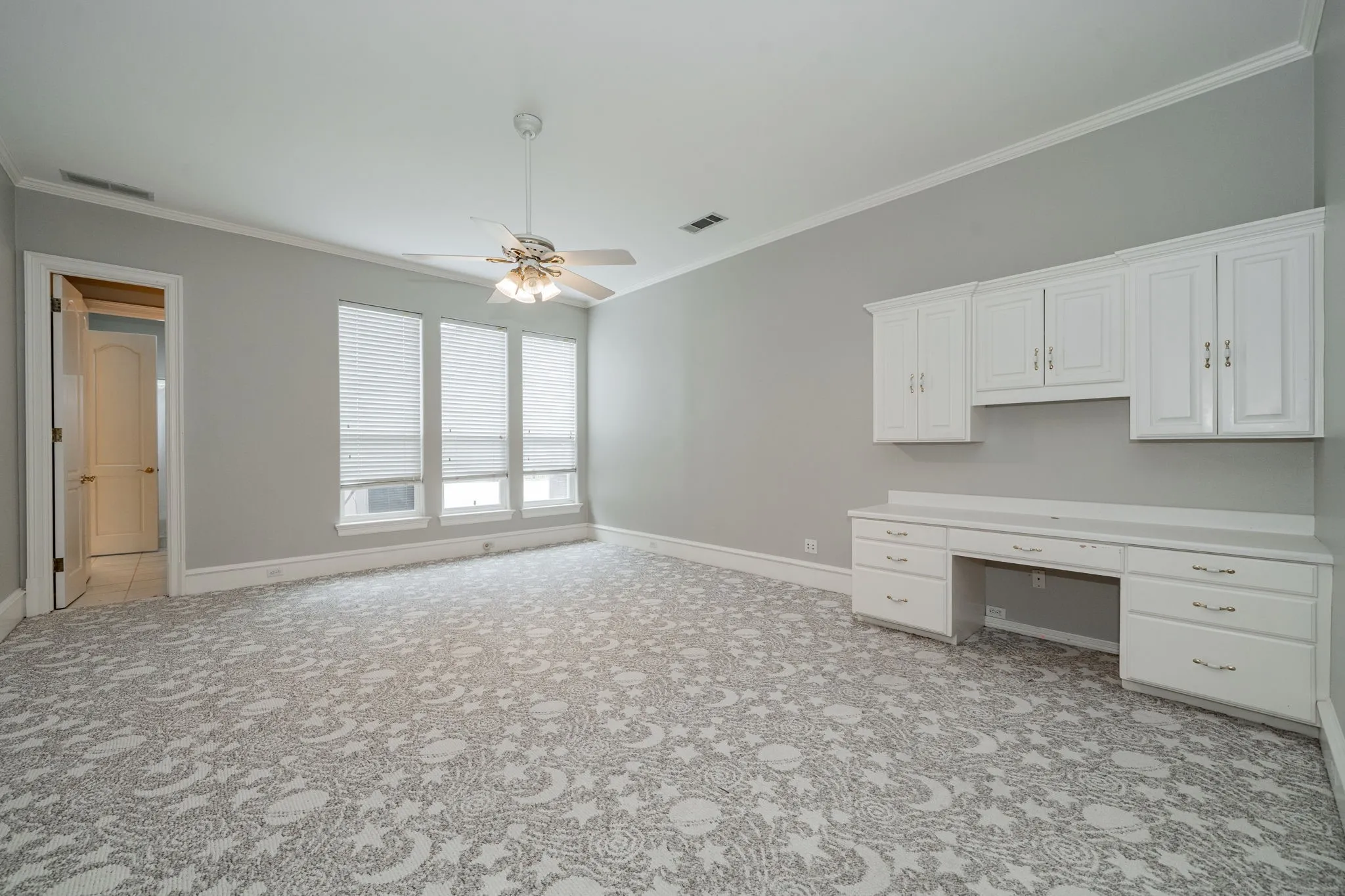 Unfurnished office featuring ornamental molding, built in desk, ceiling fan, and light carpet