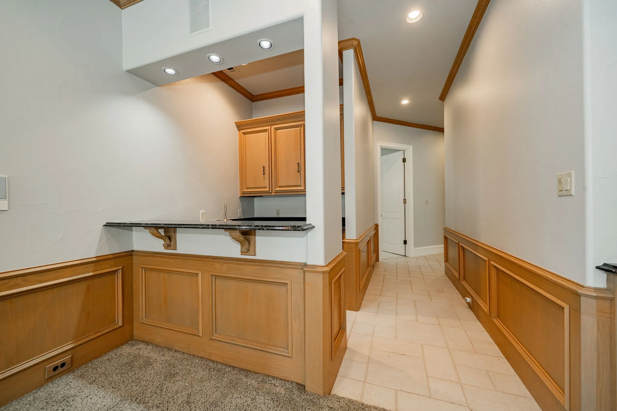 Kitchen featuring wainscoting, crown molding, recessed lighting, brown cabinets, and dark stone counters