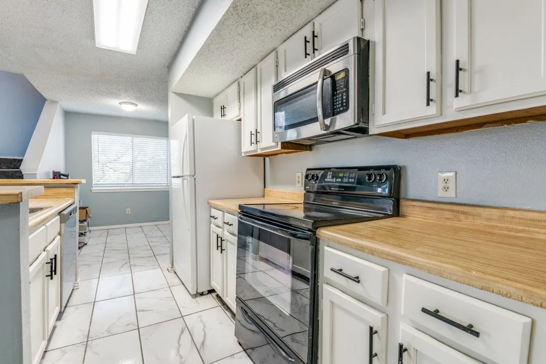 Kitchen with marble finish floor, a textured ceiling, stainless steel appliances, white cabinets, and light countertops