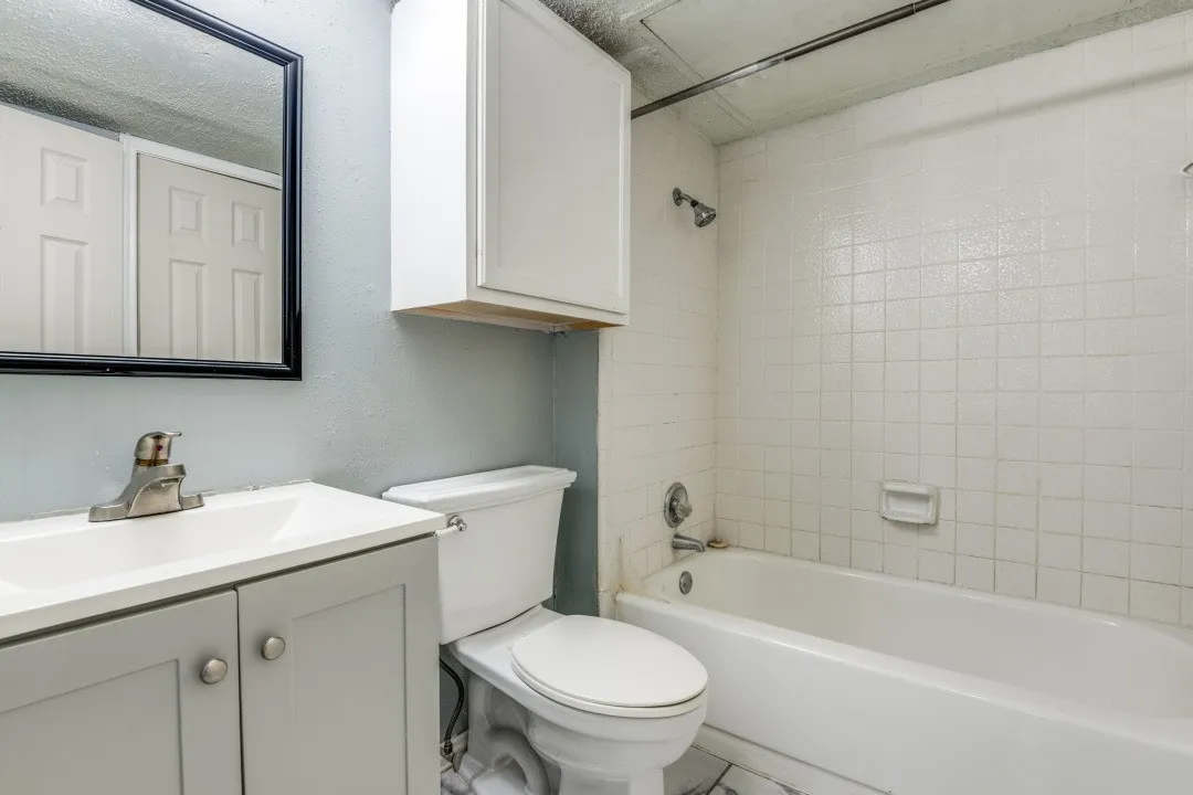 Bathroom with vanity, toilet, shower / bathtub combination, and a textured wall