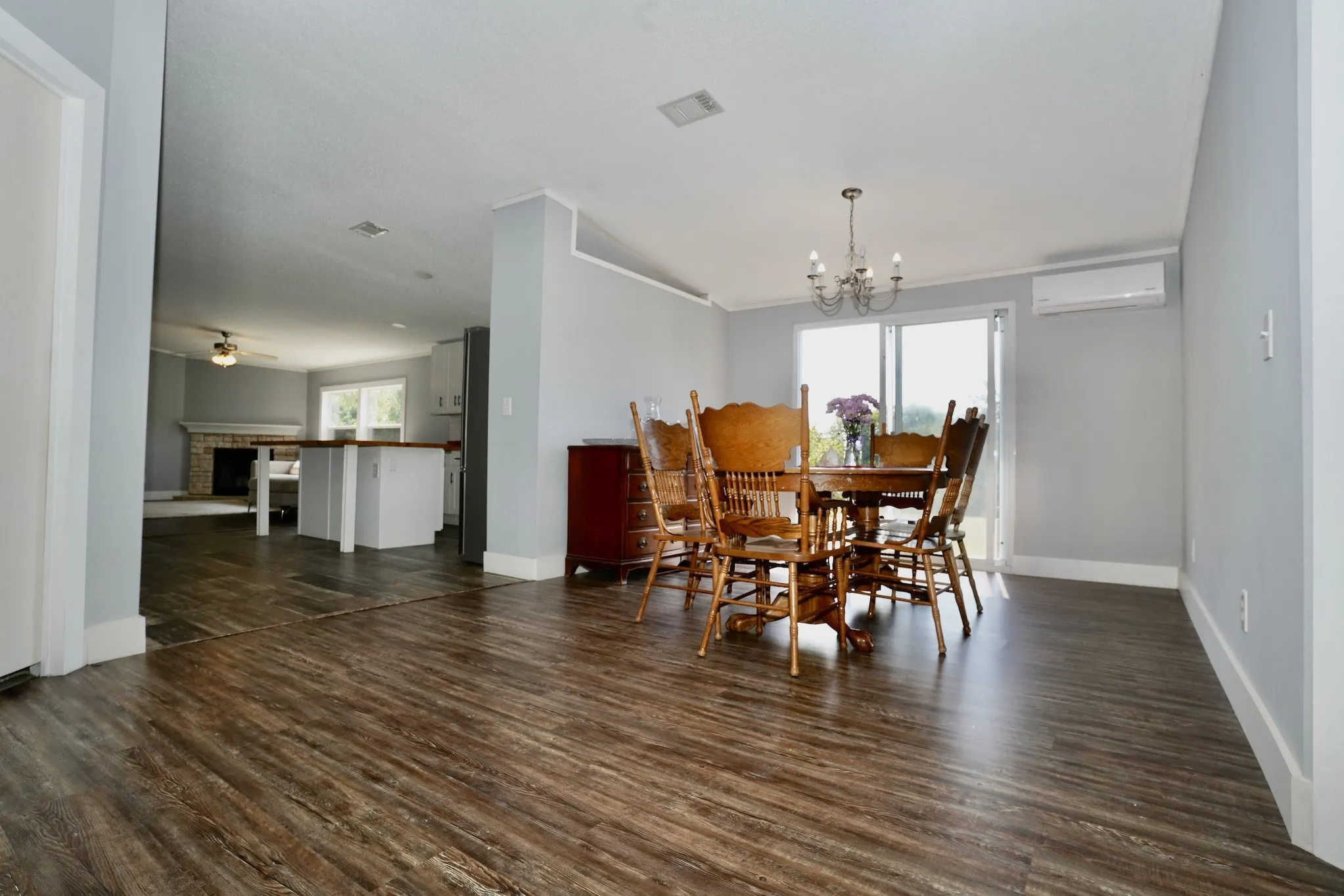 Dining area featuring dark wood-style floors, a brick fireplace, ceiling fan, a chandelier, and a wall mounted AC