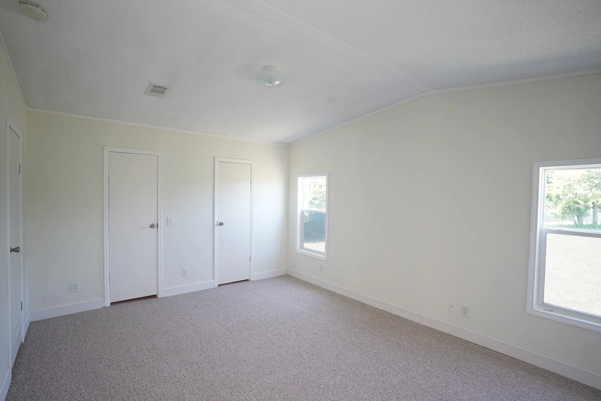 Unfurnished bedroom featuring light colored carpet, two closets, vaulted ceiling, and ornamental molding