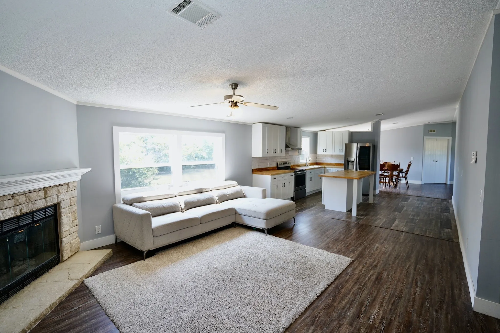 Living area with dark wood finished floors, a textured ceiling, a fireplace, and ceiling fan