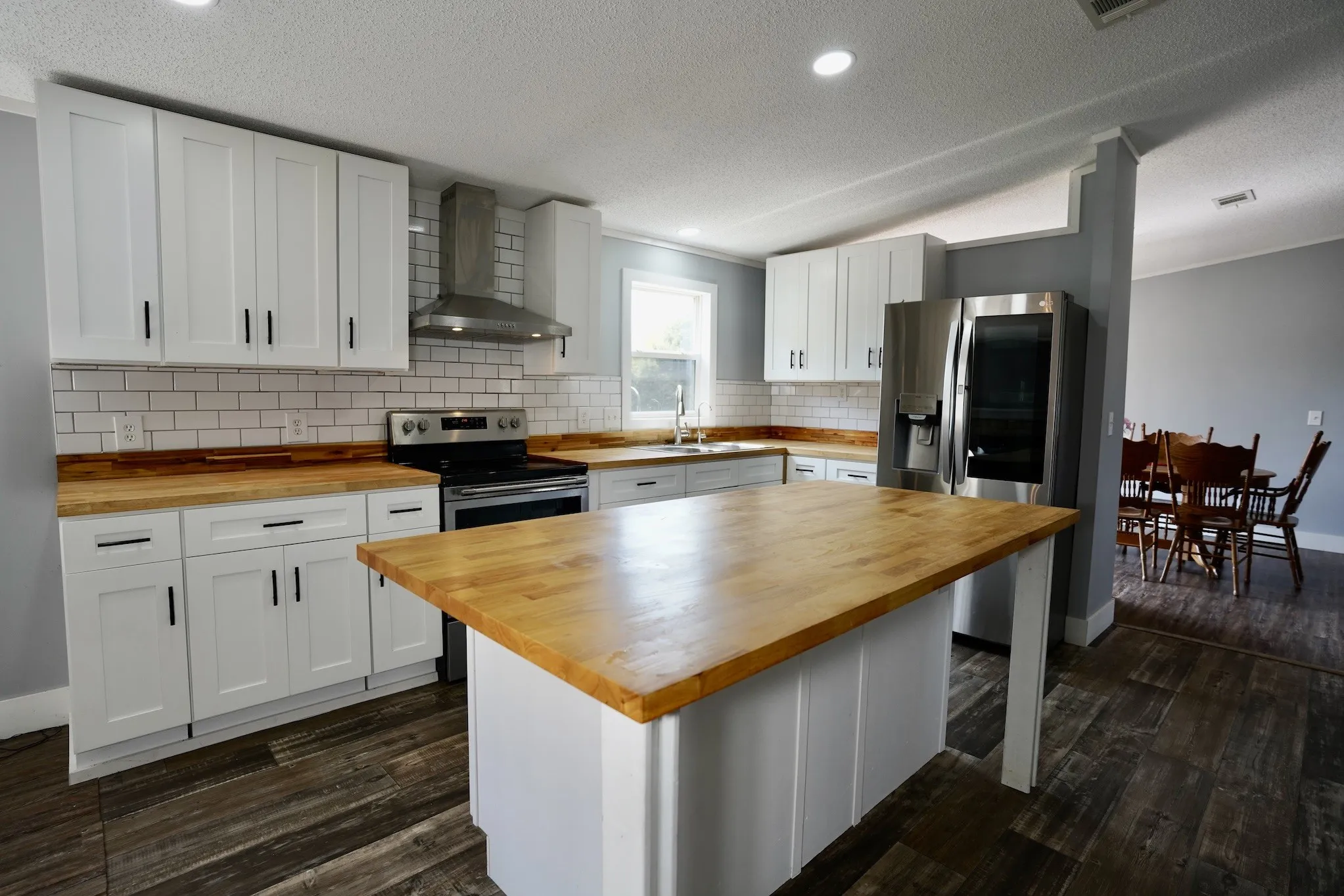 Kitchen featuring wall chimney range hood, white cabinetry, dark wood-style floors, a textured ceiling, and stainless steel appliances