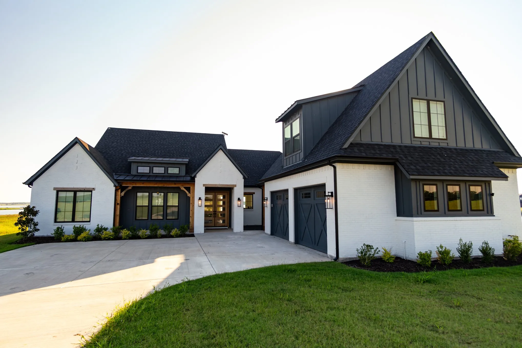 Modern inspired farmhouse with a shingled roof, brick siding, concrete driveway, board and batten siding, and a front yard
