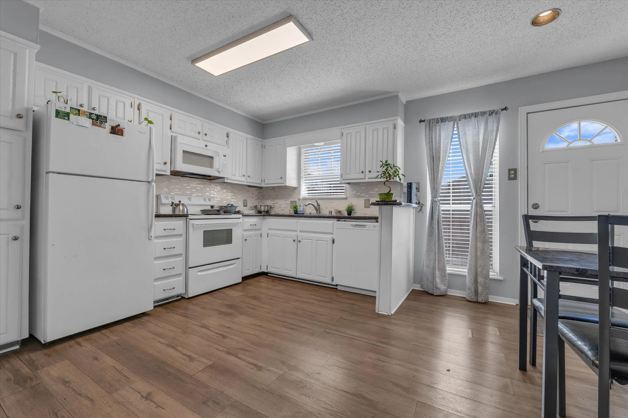 Kitchen with white appliances, white cabinetry, dark wood-type flooring, backsplash, and a textured ceiling