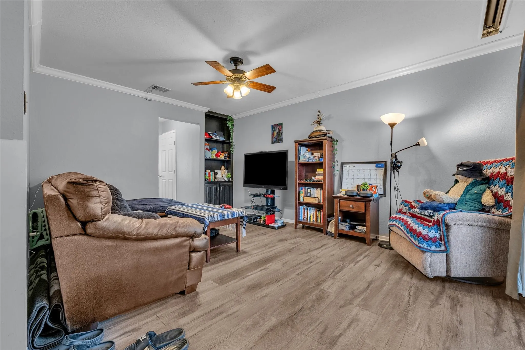 Living room with crown molding, light wood-type flooring, and a ceiling fan