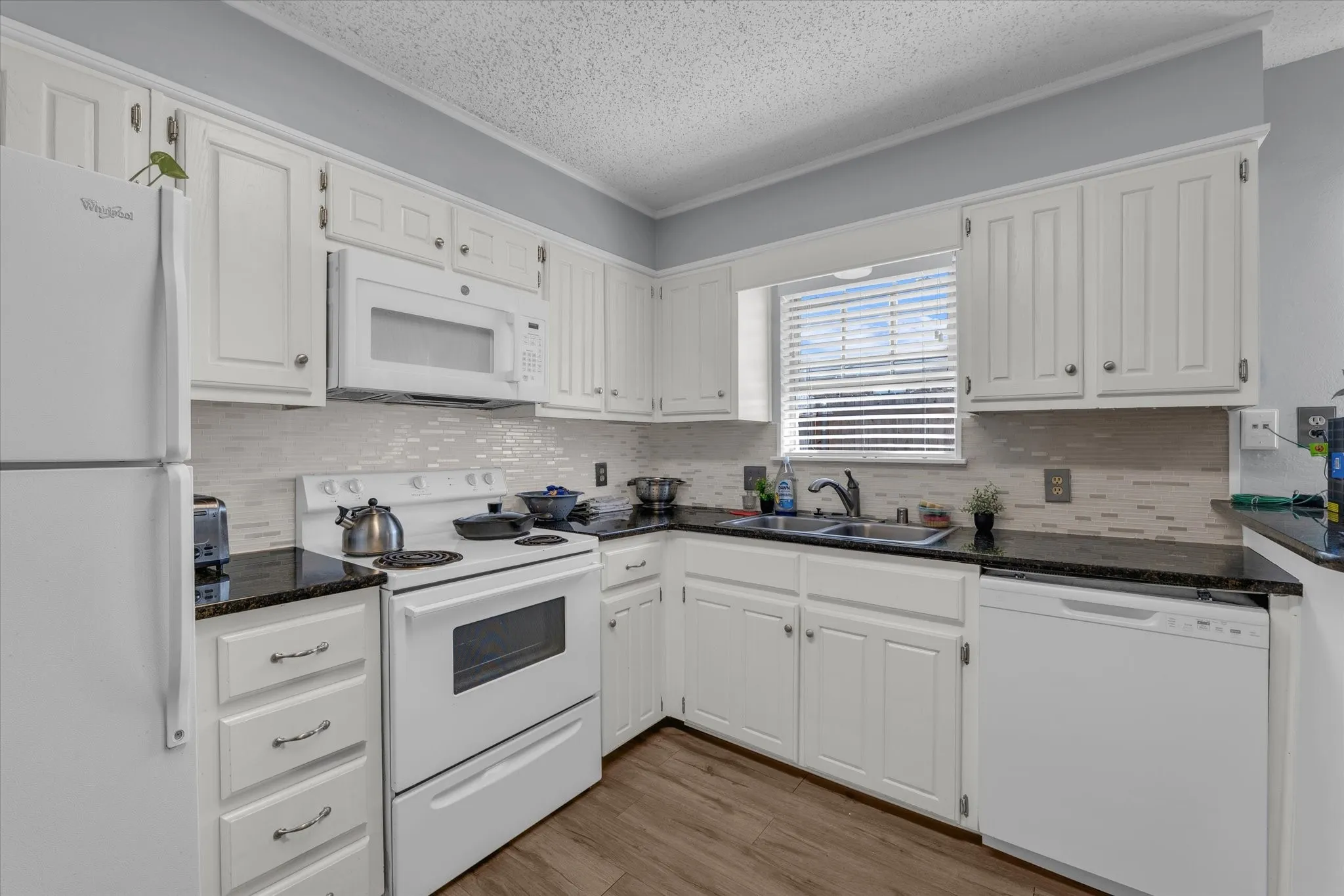 Kitchen featuring white appliances, white cabinetry, tasteful backsplash, light wood finished floors, and dark stone counters