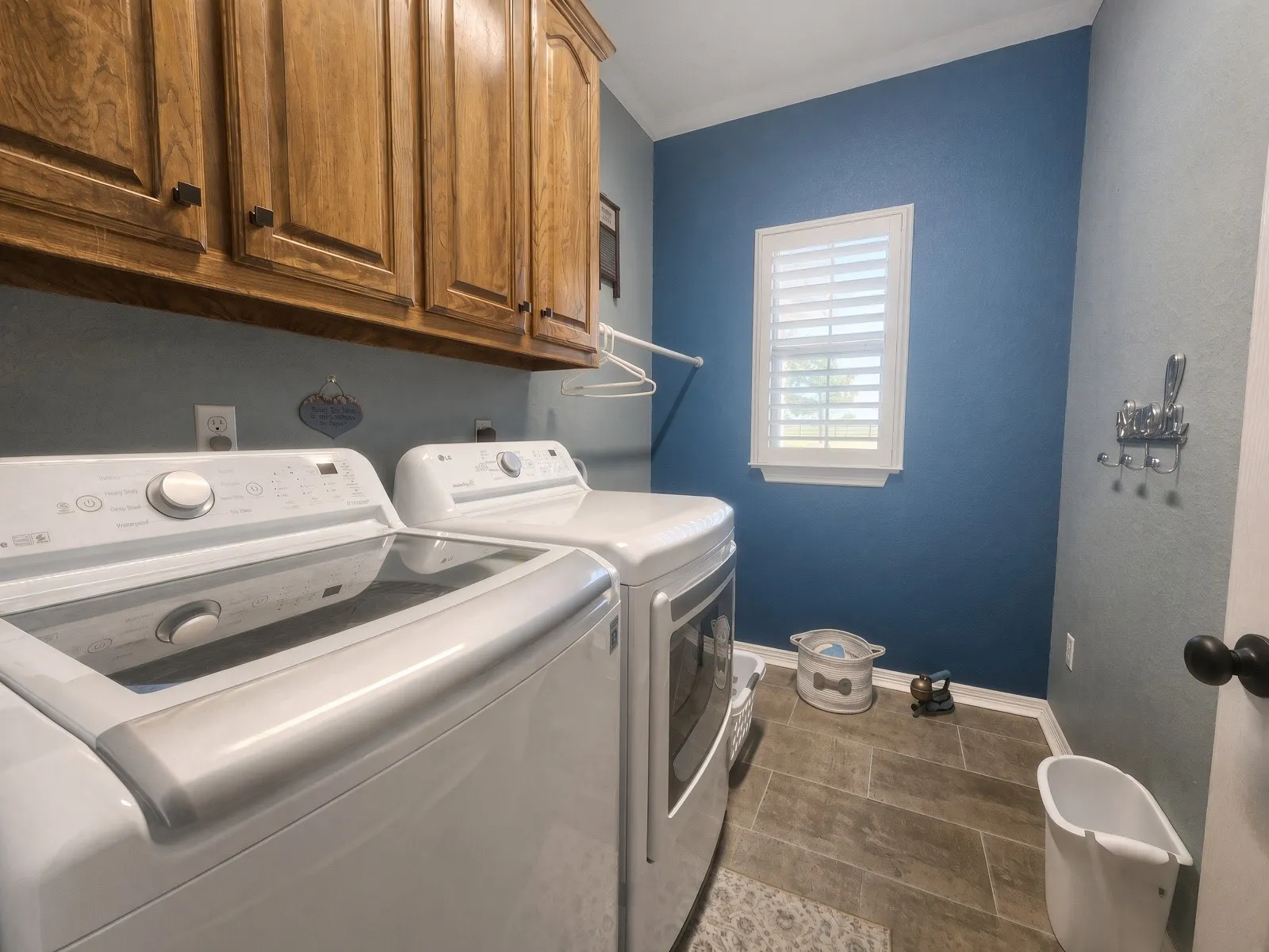 Built-in wood cabinetry, tiled flooring, window with plantation shutters, and wall-mounted drying rack