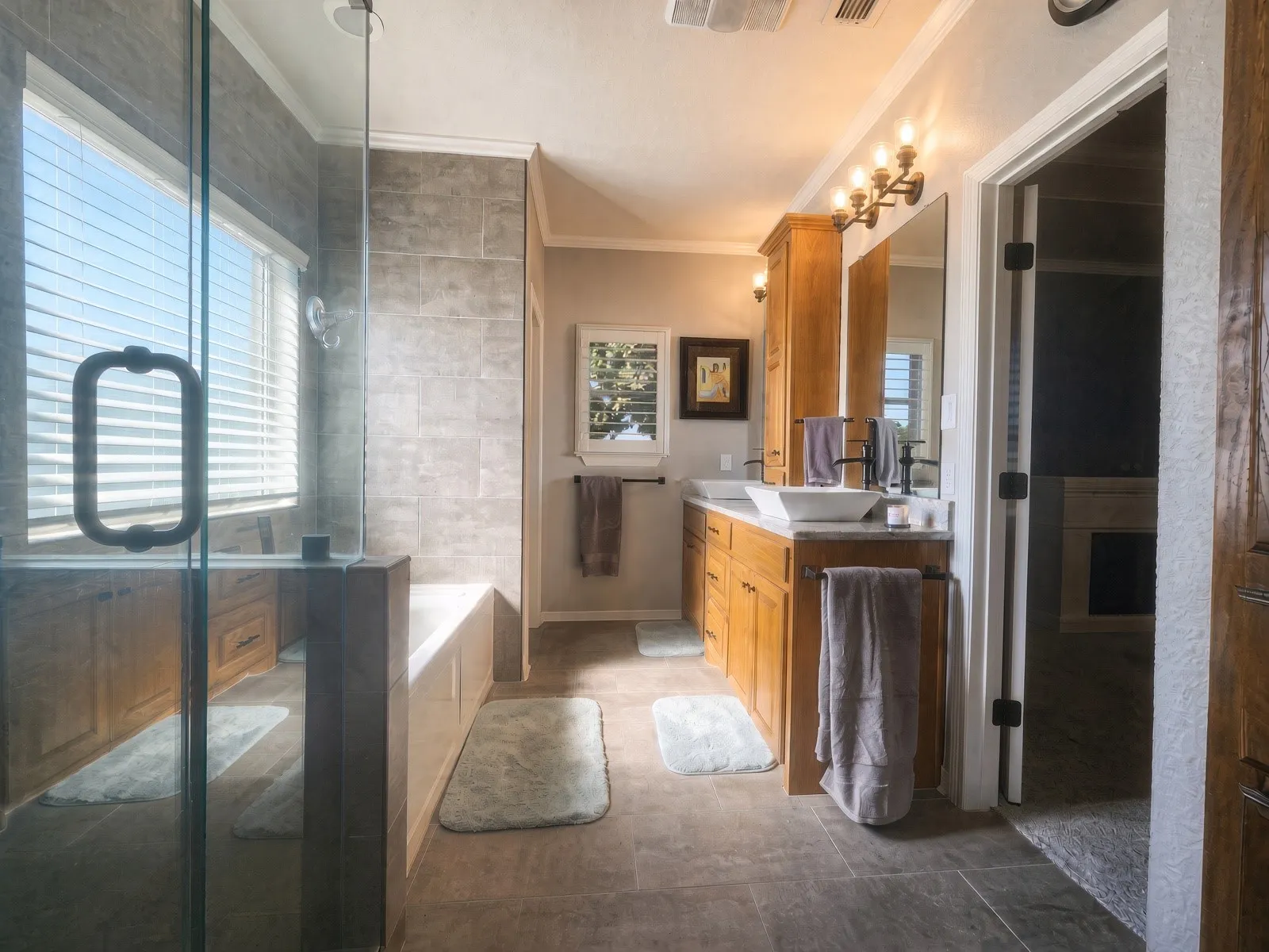 Dual vanity with vessel sinks, wood-finish cabinetry, tile flooring, glass-enclosed shower, and built-in bathtub