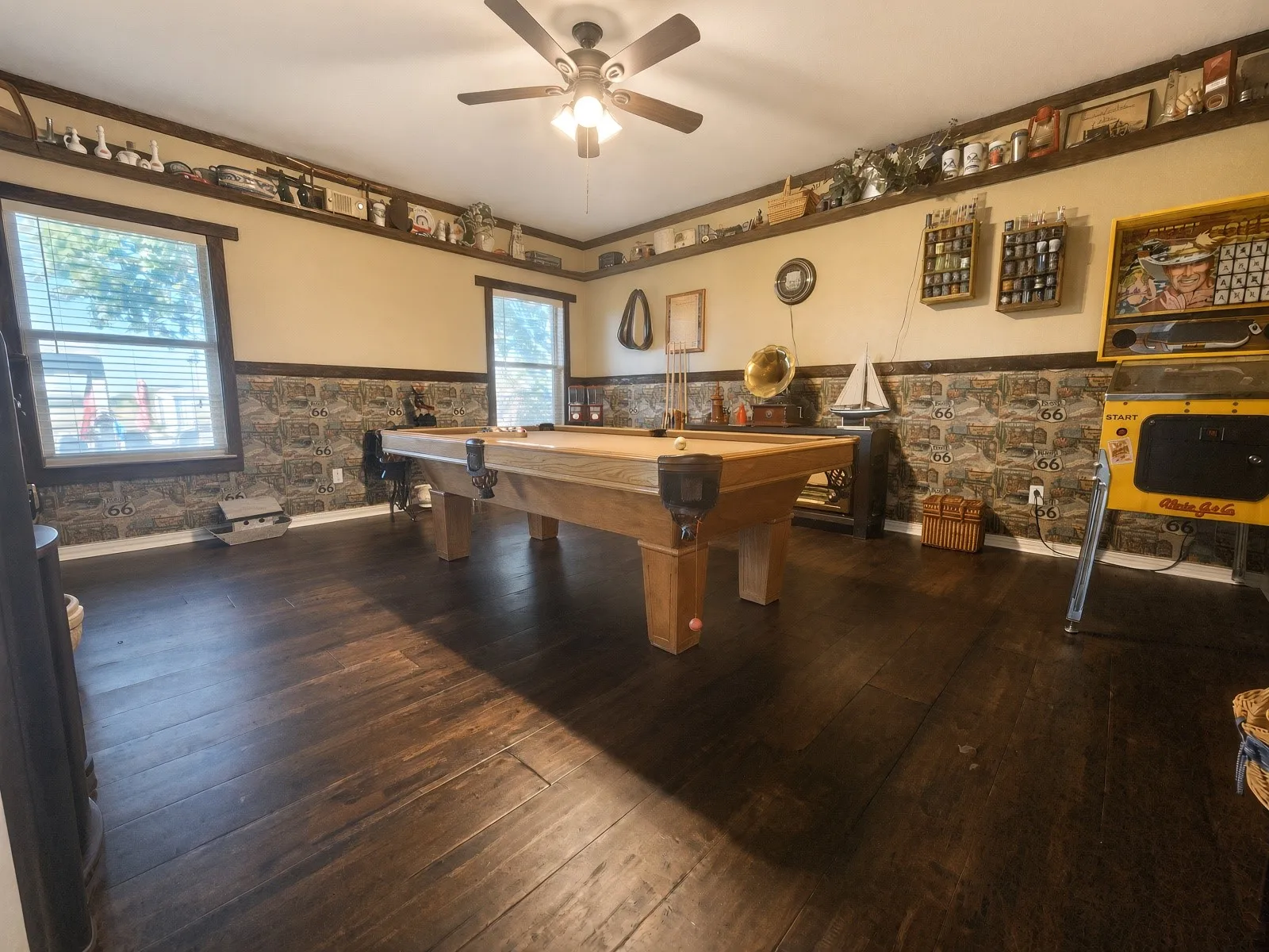 Dark wood-finish flooring, stone-finish wainscoting, and a ceiling fan with integrated lighting