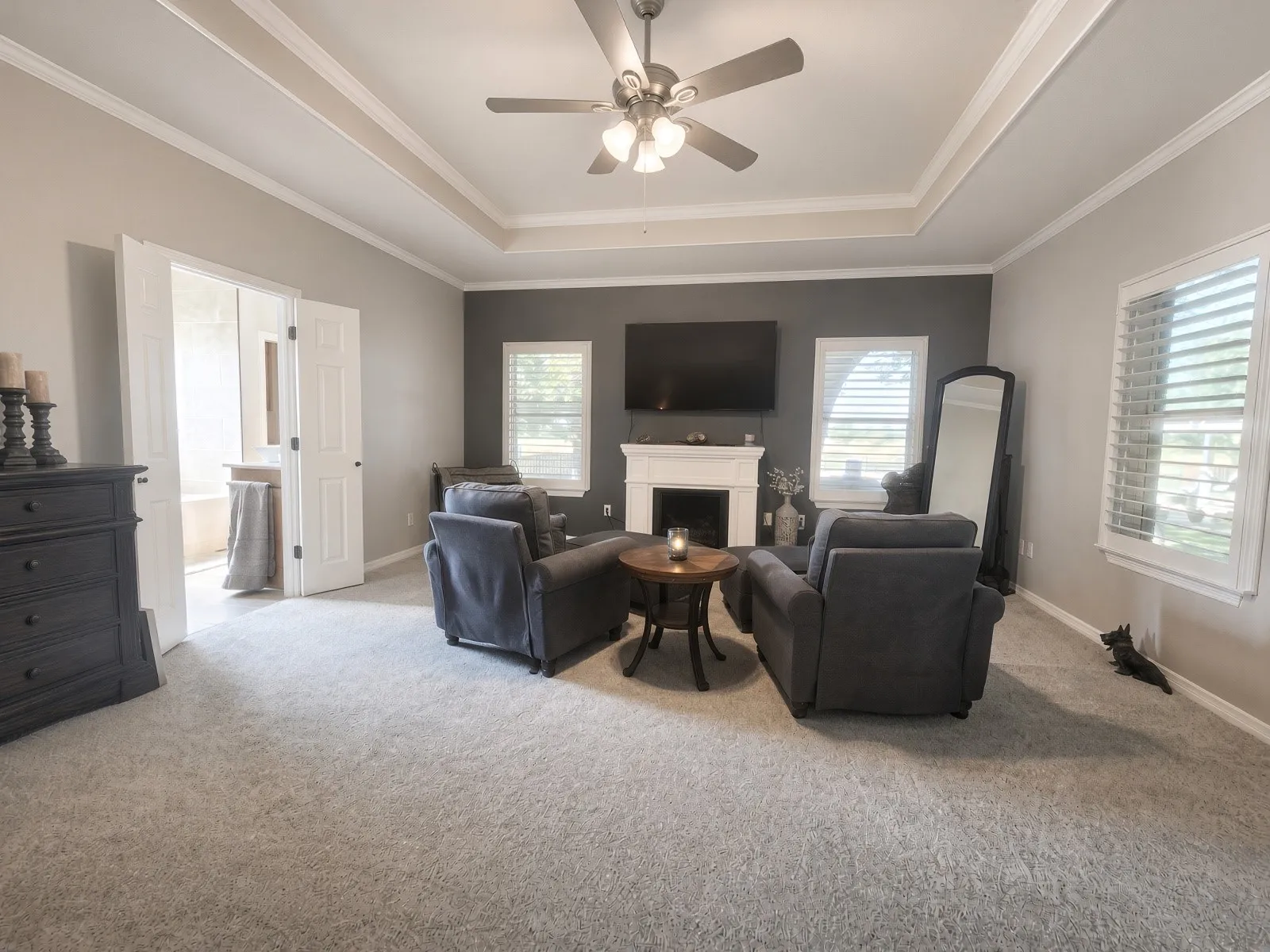 Recessed tray ceiling with crown molding, white fireplace with mantle, dual interior doors, and white plantation shutters