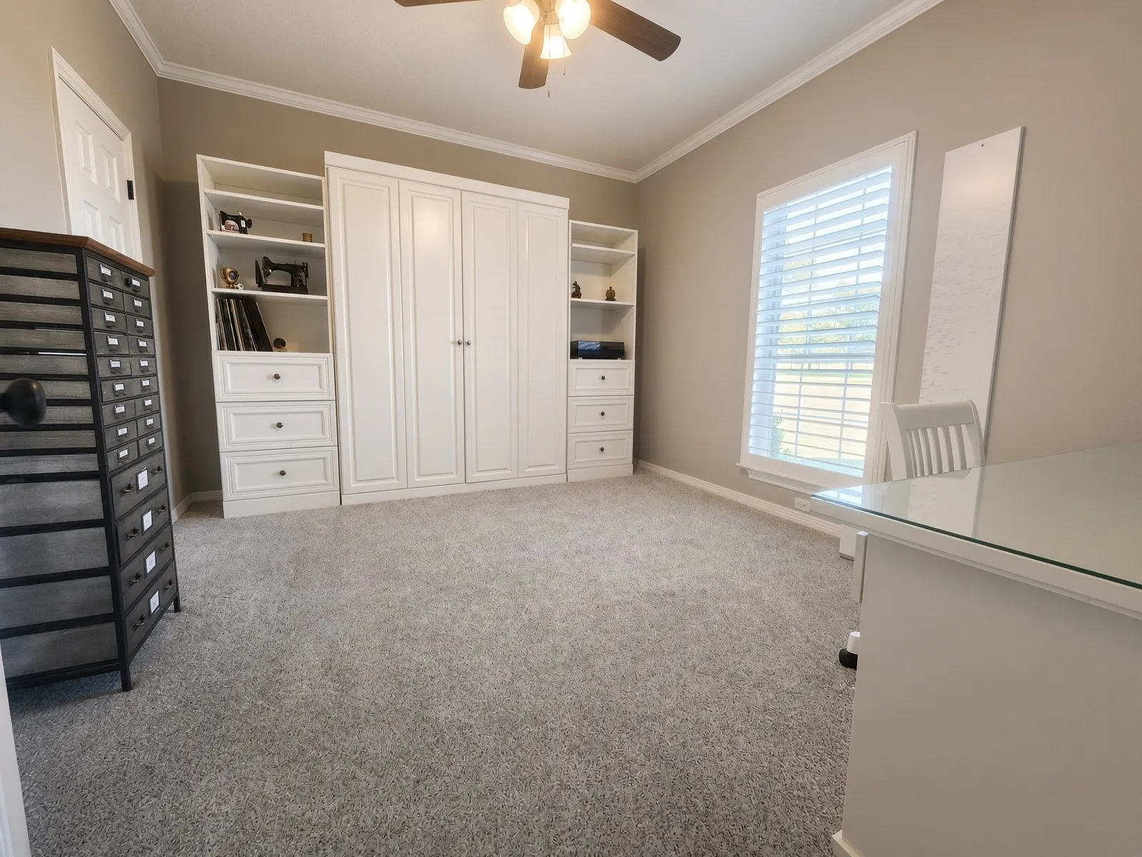 Built-in cabinetry with open shelving and drawers, ceiling fan, crown molding, and window with blinds