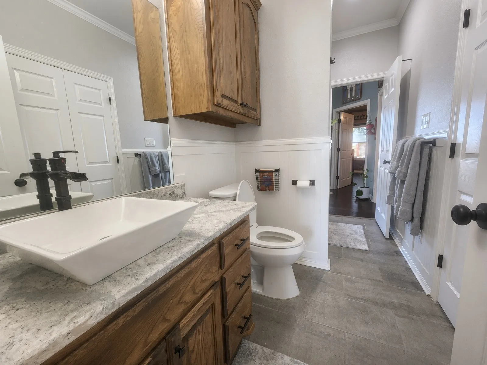 Wood-finish vanity with a rectangular vessel sink, stone-finish countertop, and wall-mounted faucet