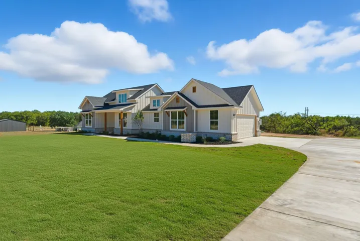 View of front of house featuring board and batten siding, a front lawn, driveway, covered porch, and roof with shingles