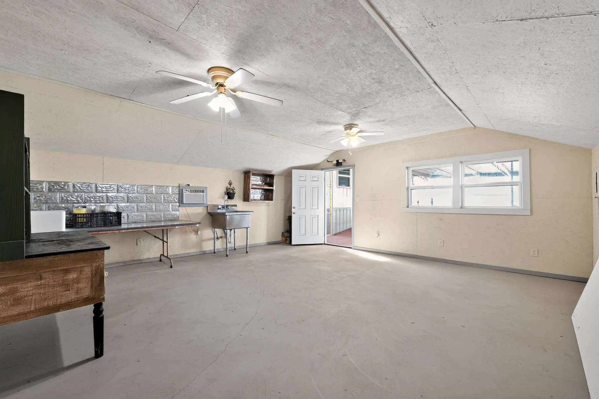 Living area with lofted ceiling, a ceiling fan, unfinished concrete floors, and a wall mounted air conditioner