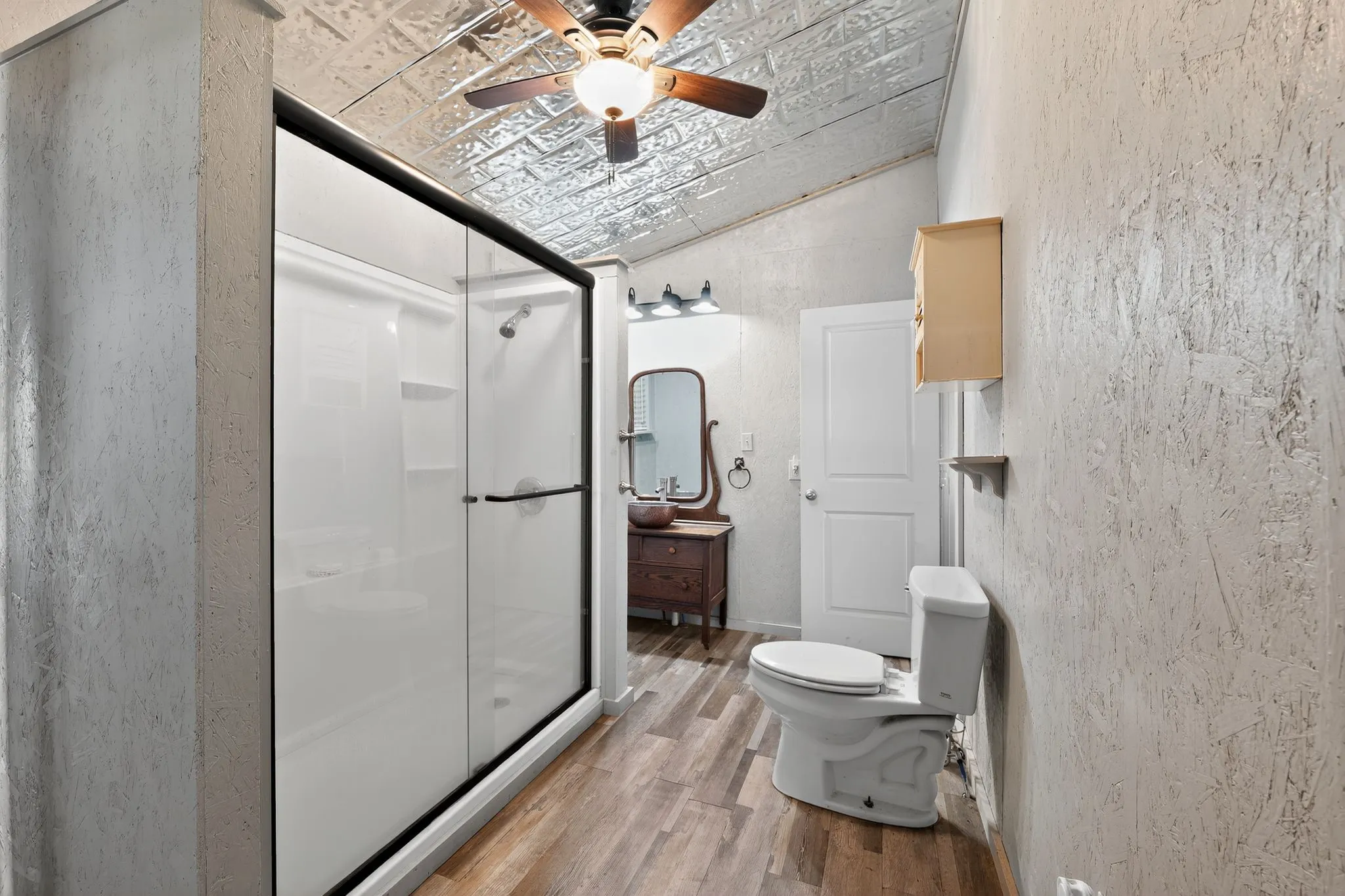 Full bathroom with a shower stall, lofted ceiling, light wood-type flooring, a textured wall, and a ceiling fan