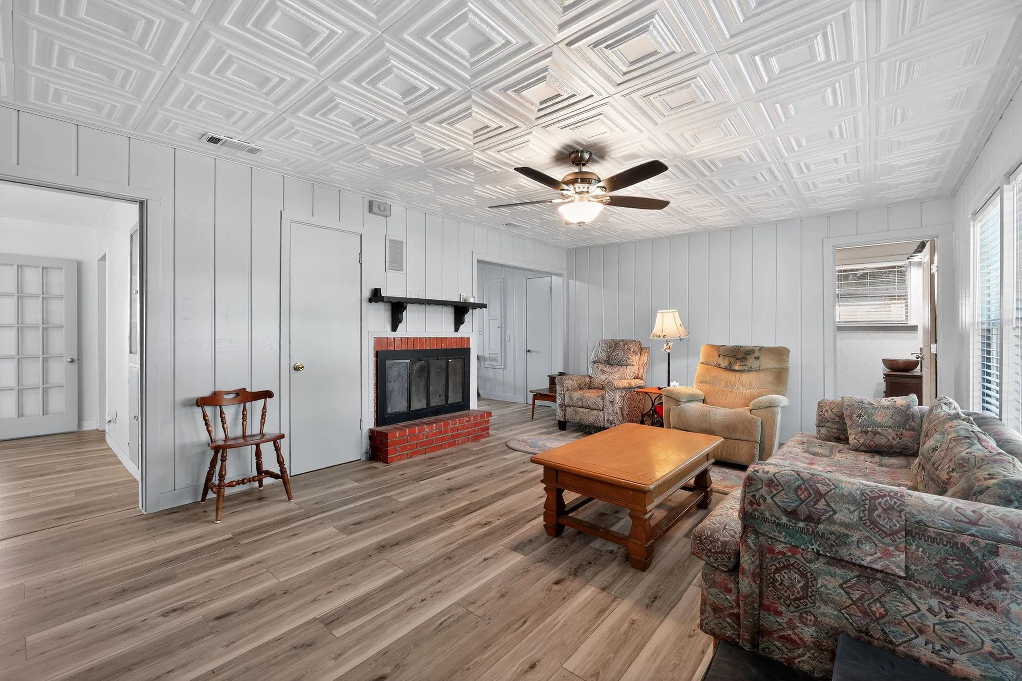 Living area featuring an ornate ceiling, light wood-style flooring, a brick fireplace, and ceiling fan