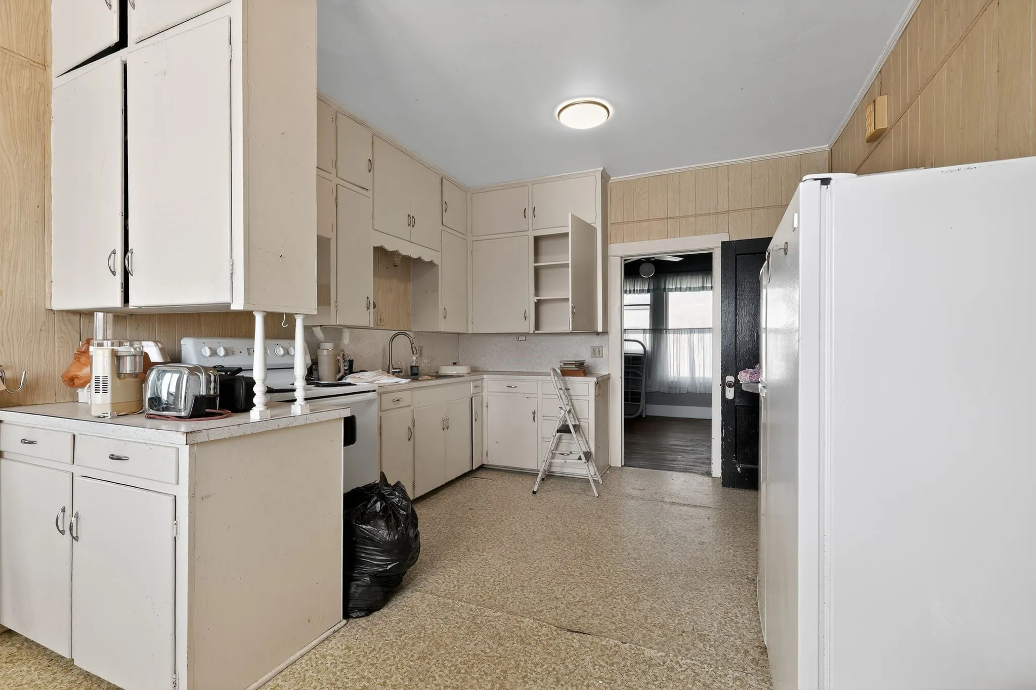 Kitchen with white appliances, light countertops, wooden walls, open shelves, and cream cabinetry
