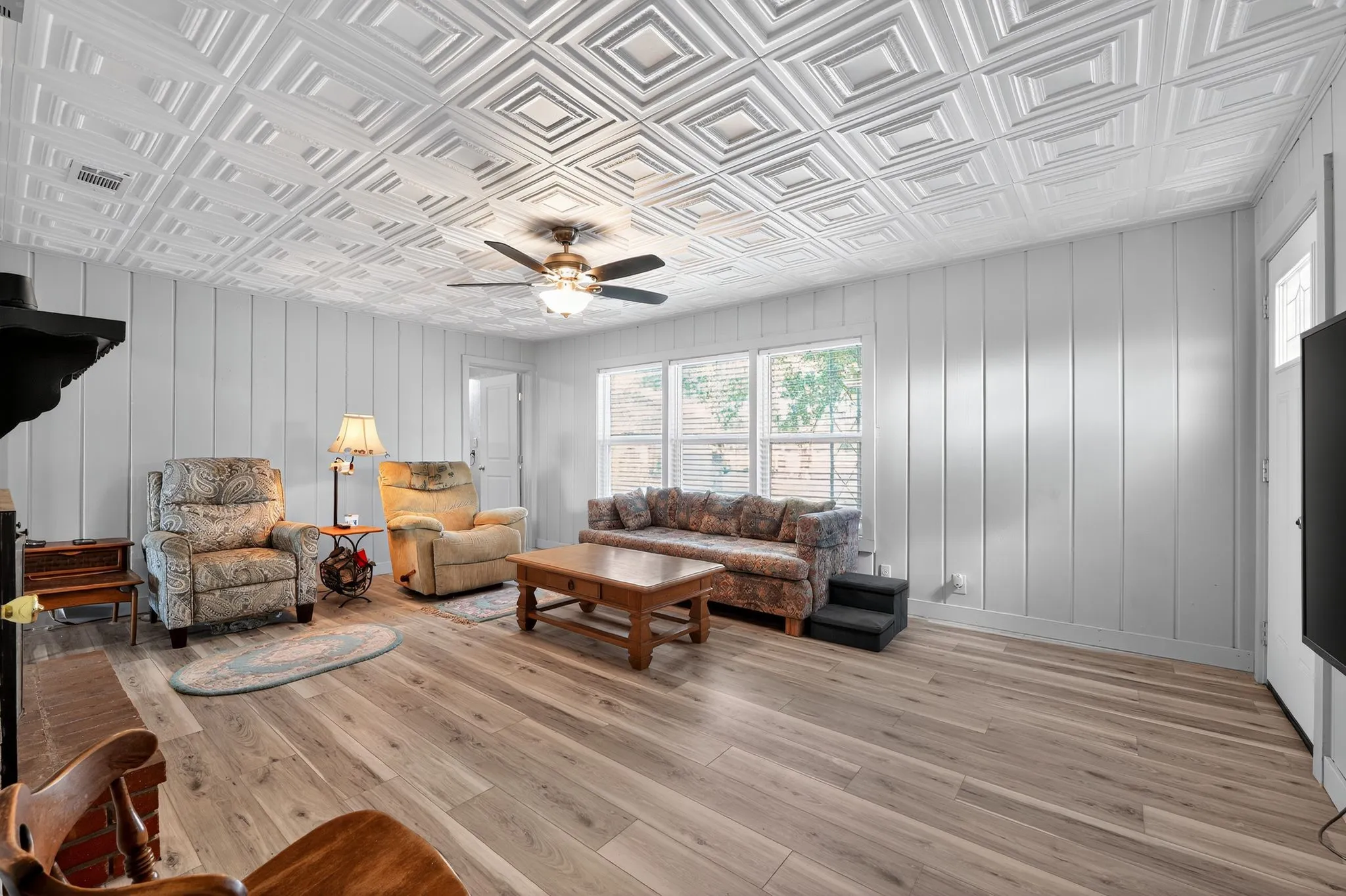 Living area featuring plenty of natural light, a ceiling fan, an ornate ceiling, light wood finished floors, and wood walls