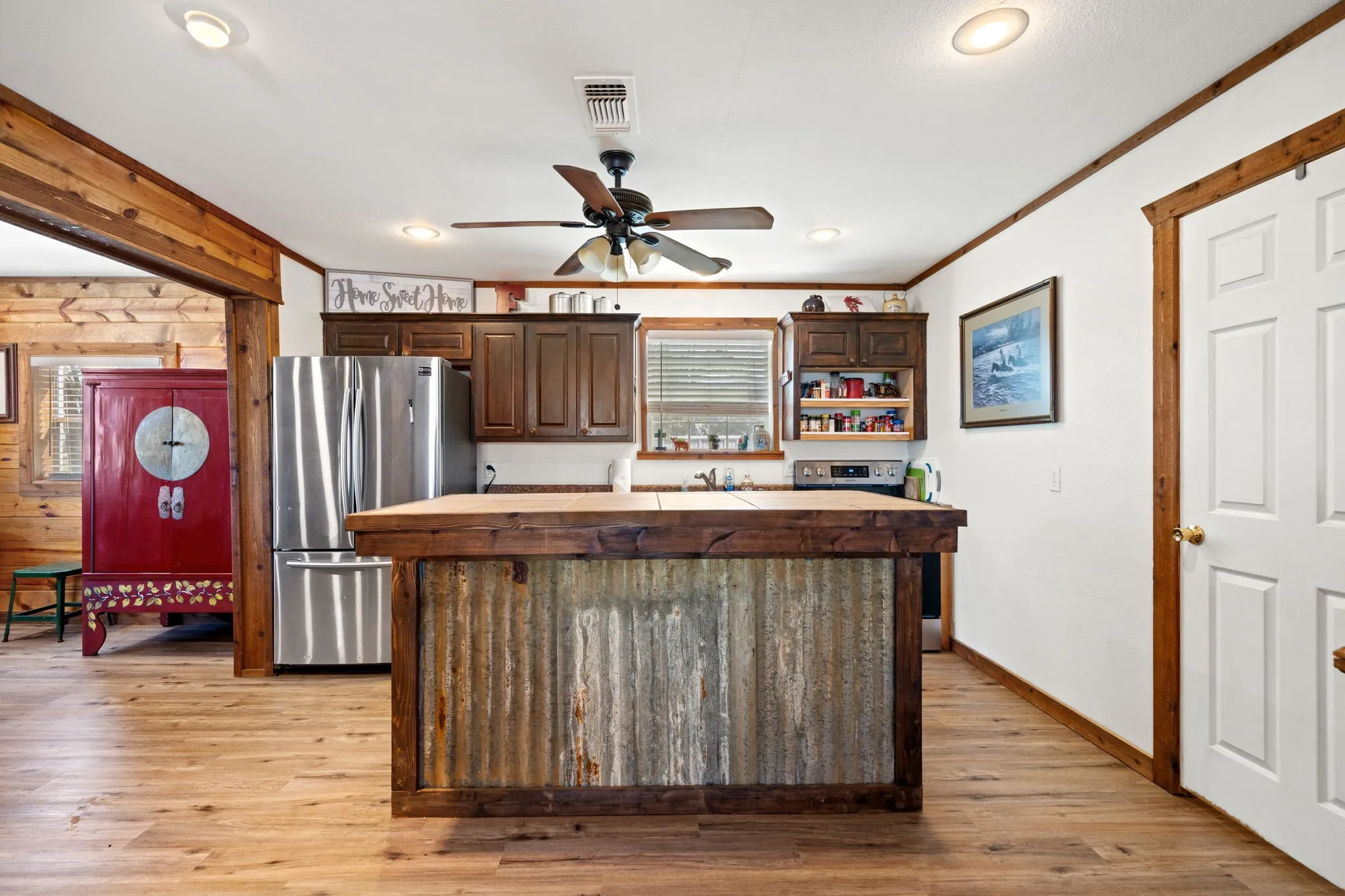Kitchen with dark brown cabinetry, freestanding refrigerator, a center island, light wood-type flooring, and wood walls