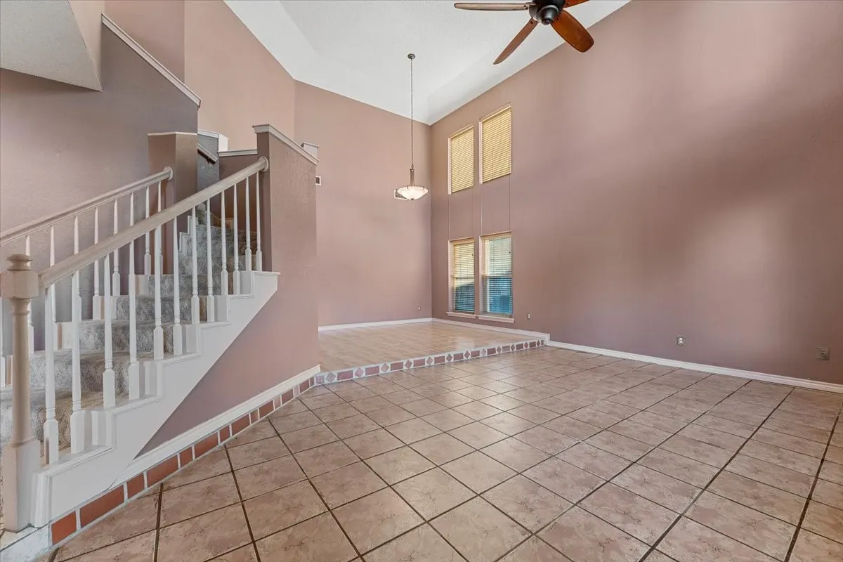 Unfurnished room featuring light tile patterned floors, a high ceiling, a ceiling fan, and stairs